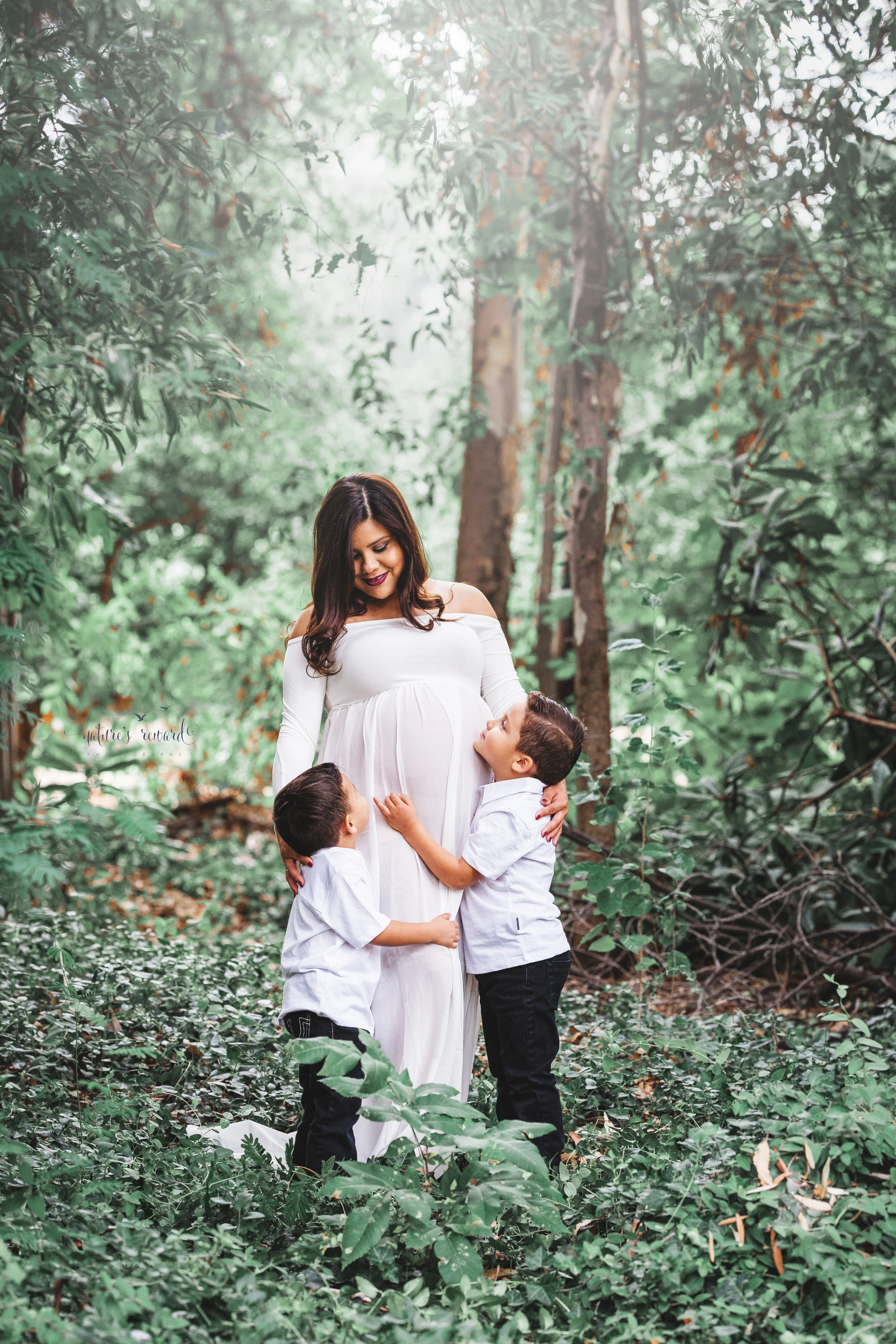 Gorgeous family in whites in a lush green park celebrate the upcoming arrival of their new family member in this lovely maternity session portrait by Nature’s Reward Photography