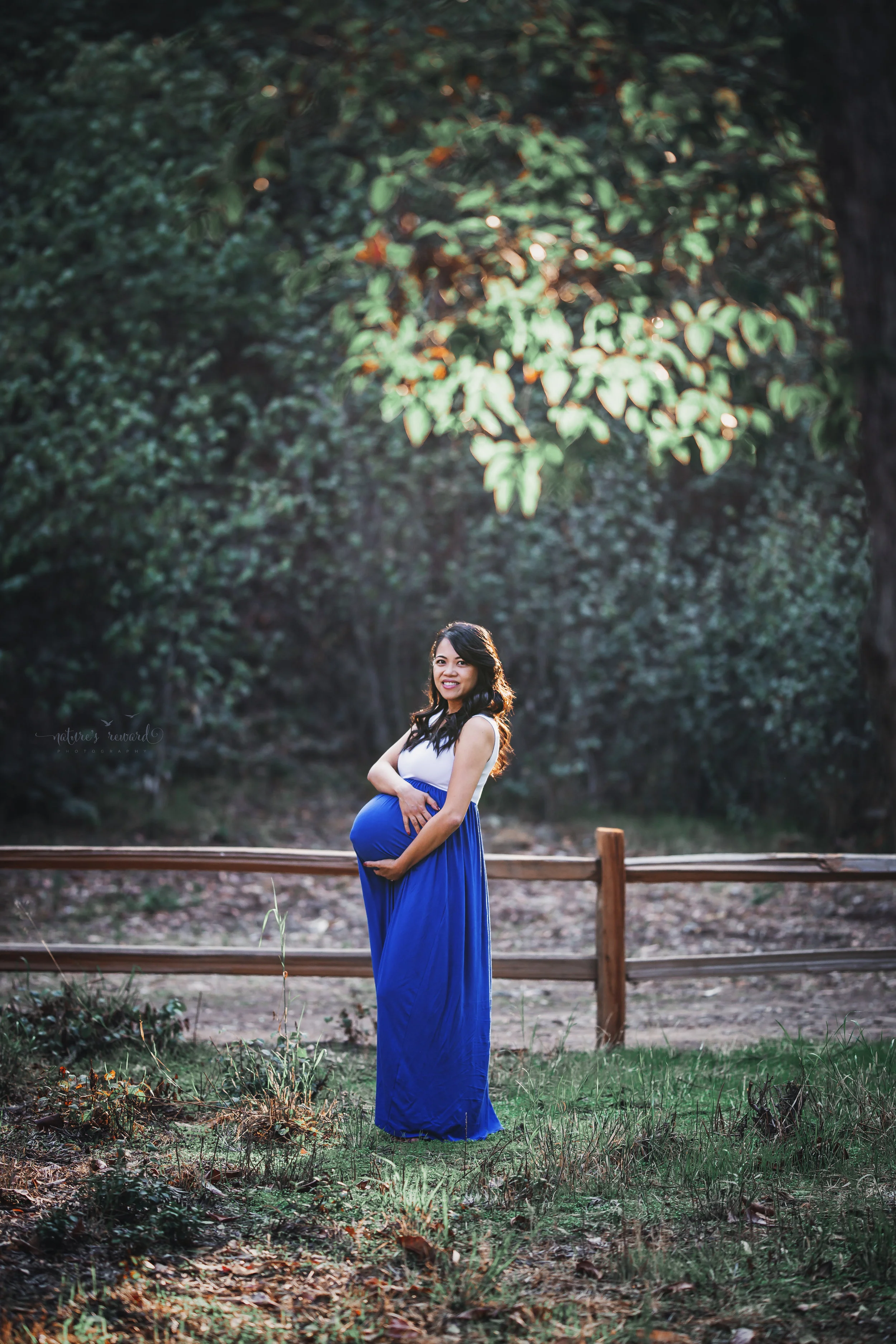 Beautiful full term expecting mother in white and blue dress in a park setting in this maternity session portrait by Nature’s Reward Photography