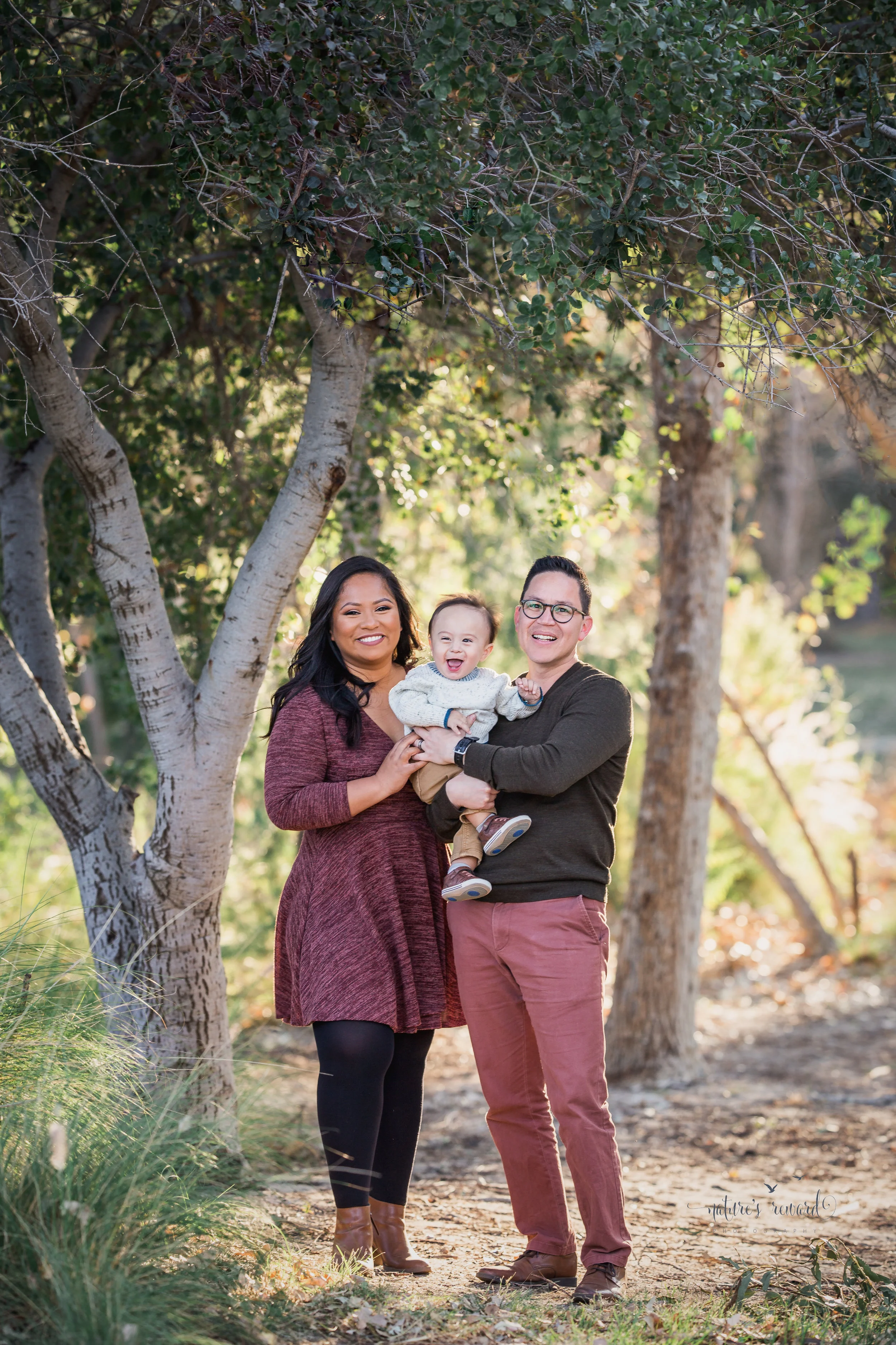 Aunty and uncle proudly hold their nephew in a park setting a portrait by Nature’s Reward Photography