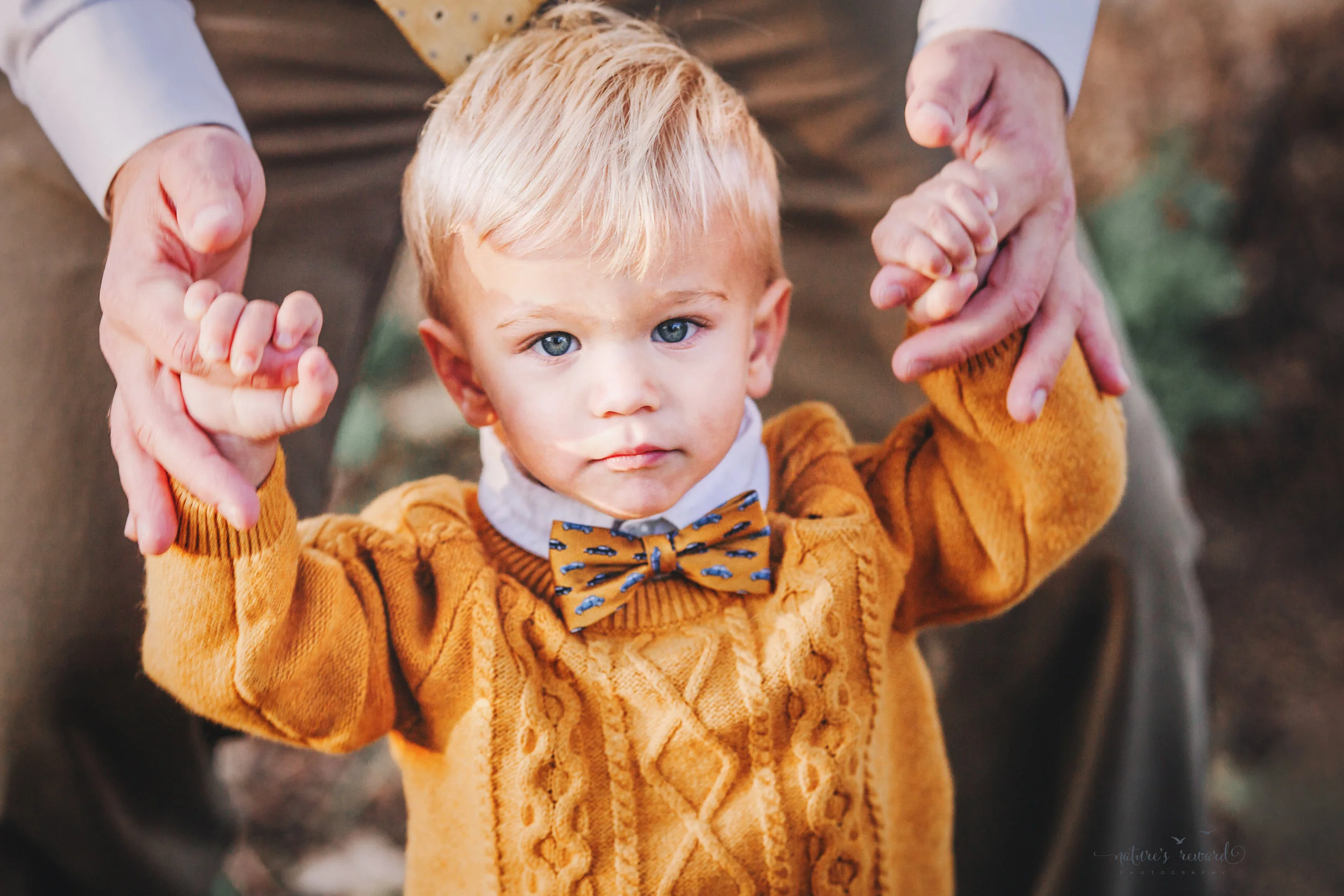 Baby Boy in daddy hands in a yellow sweater and cute bow tie- A portrait By Nature’s Reward Photography!