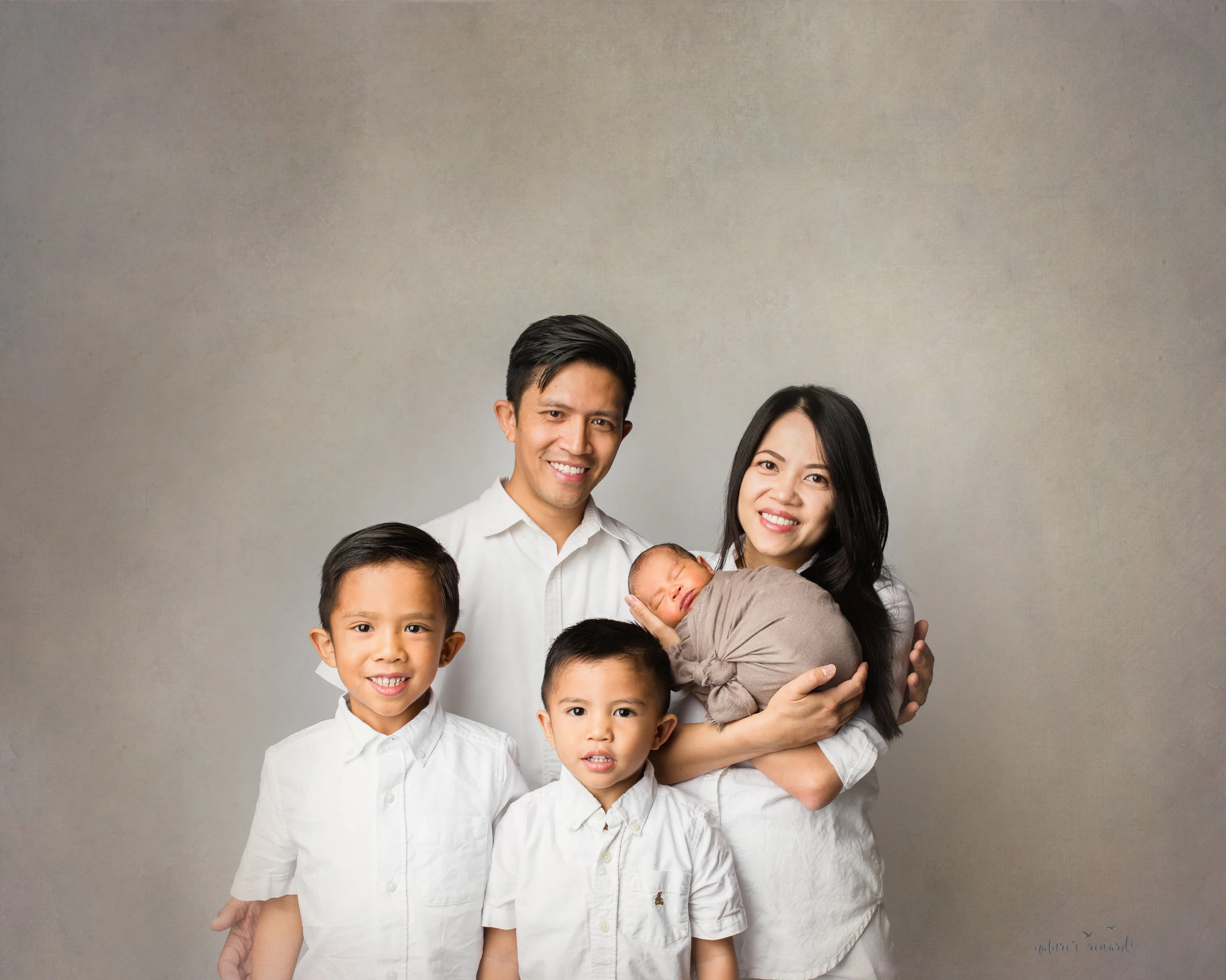 A newborn baby boy and his family in whites, and tans, a portrait by Nature’s Reward Photography