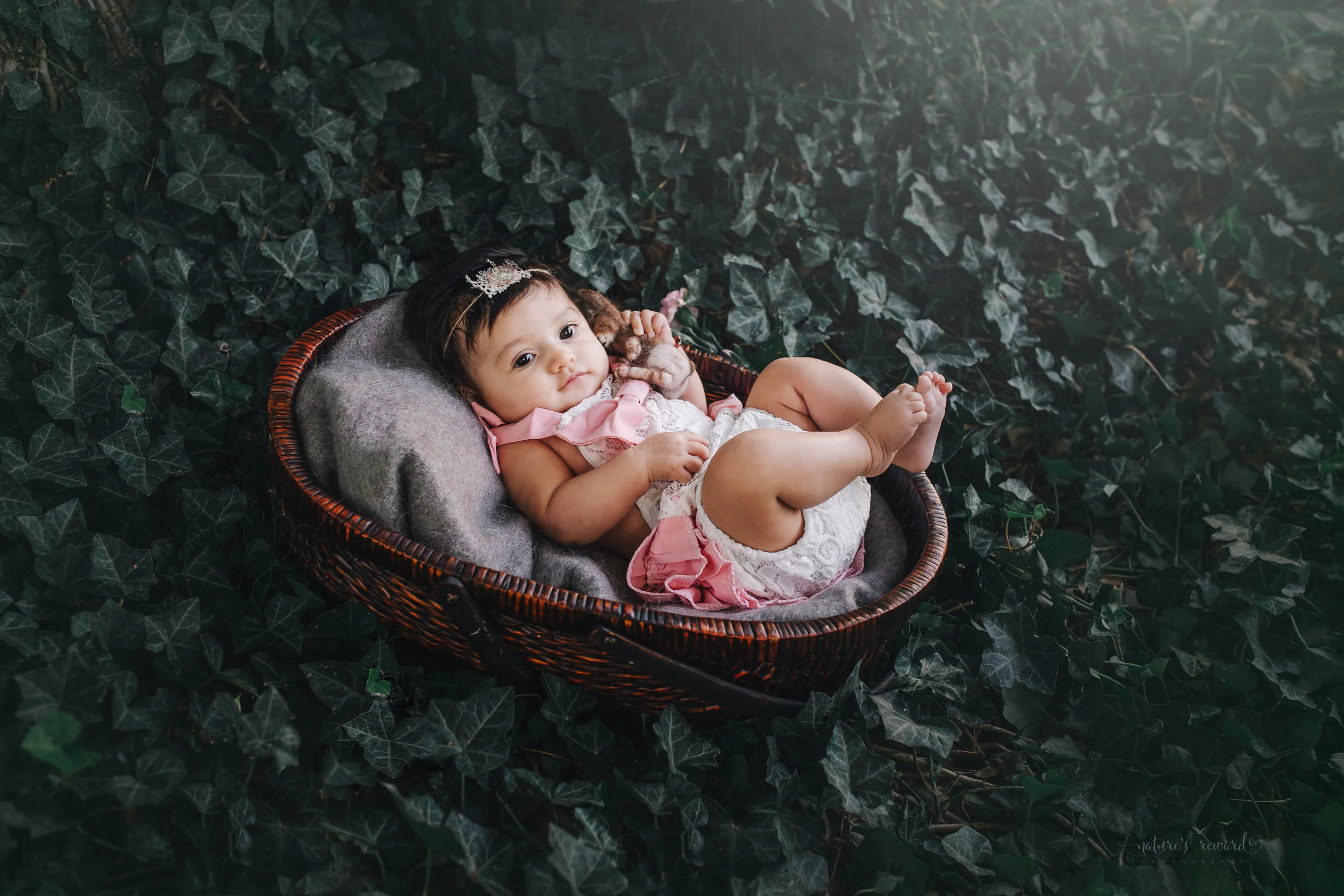 Lovely 10 week old newborn baby girl sin a darling white and pink outfit, in a bed of ivy- a portrait by Nature’s Reward Photography