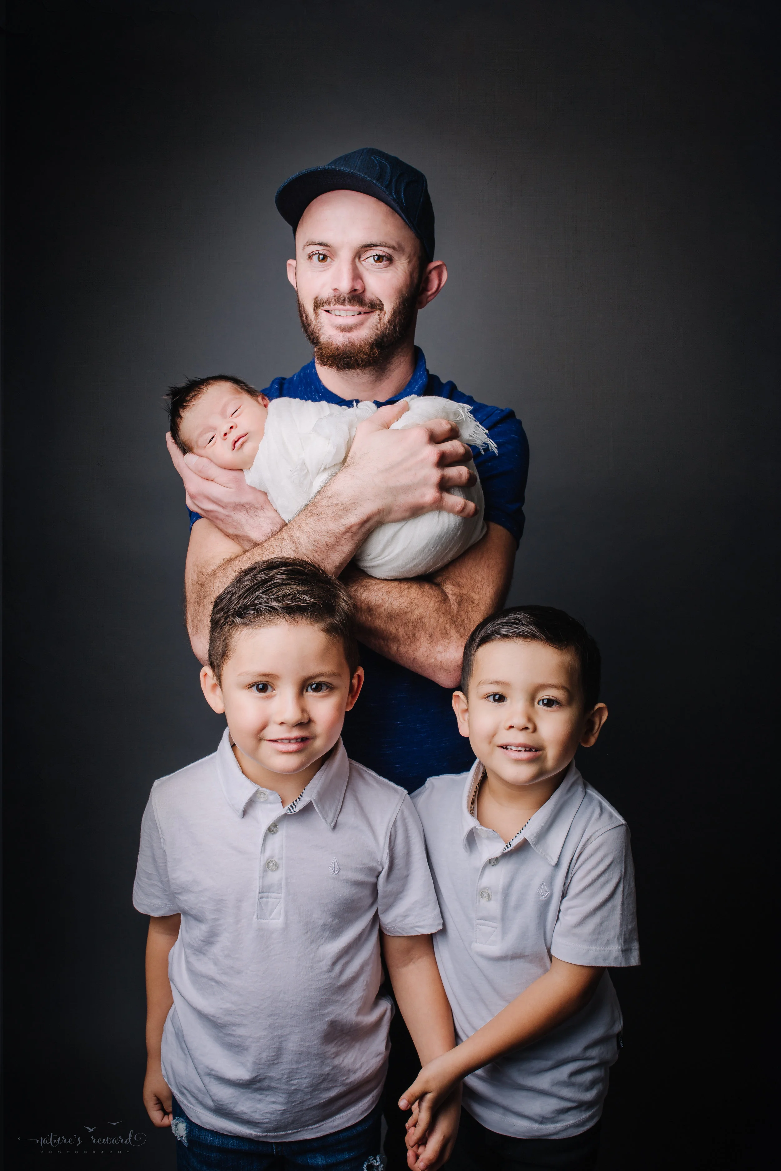 Newborn Baby Boy swaddled in white with his father and two big brothers - a portrait by Nature’s Reward Photography