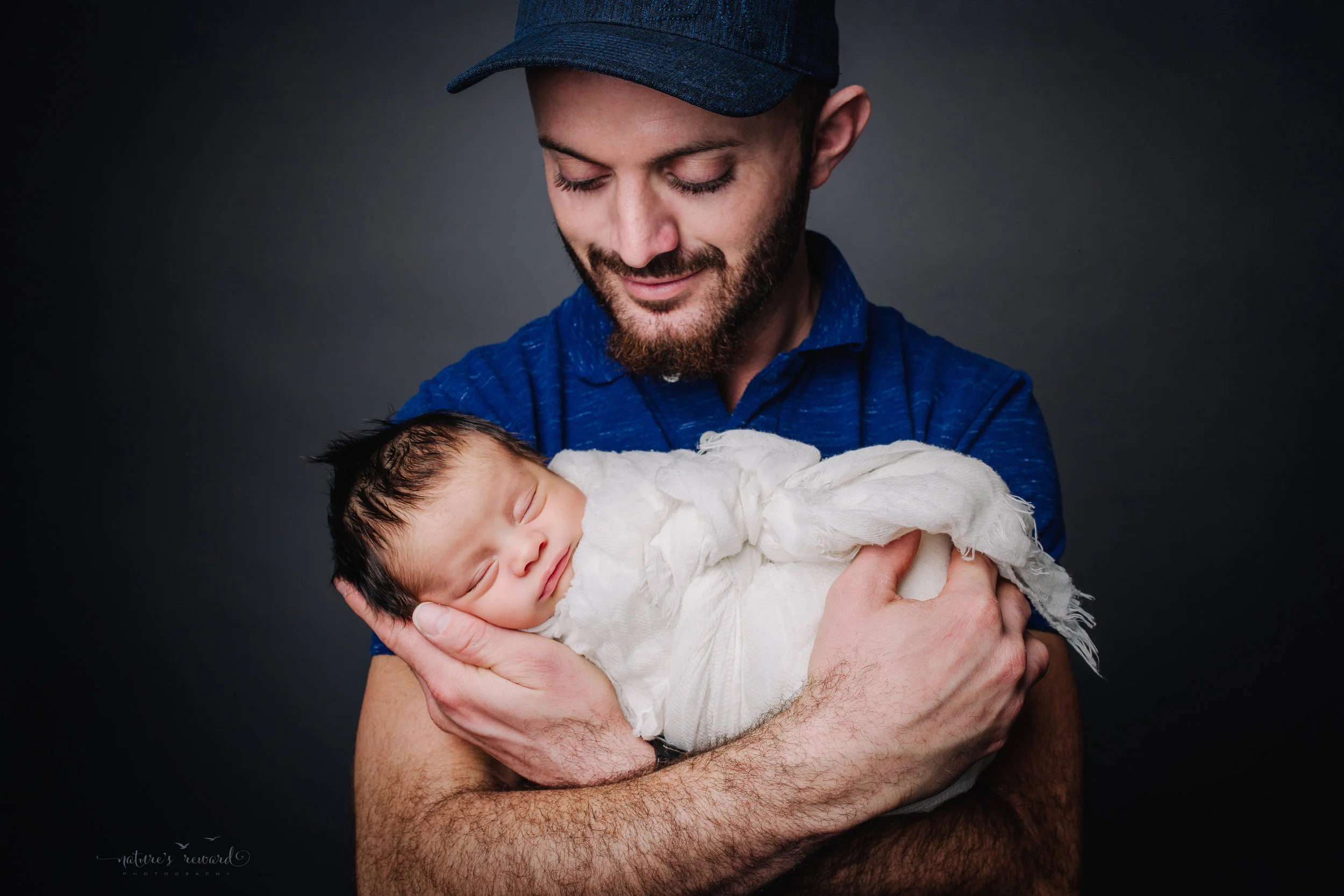 Newborn Baby boy swaddled in white in his happy father’s arms - a portrait by Nature’s Reward Photography