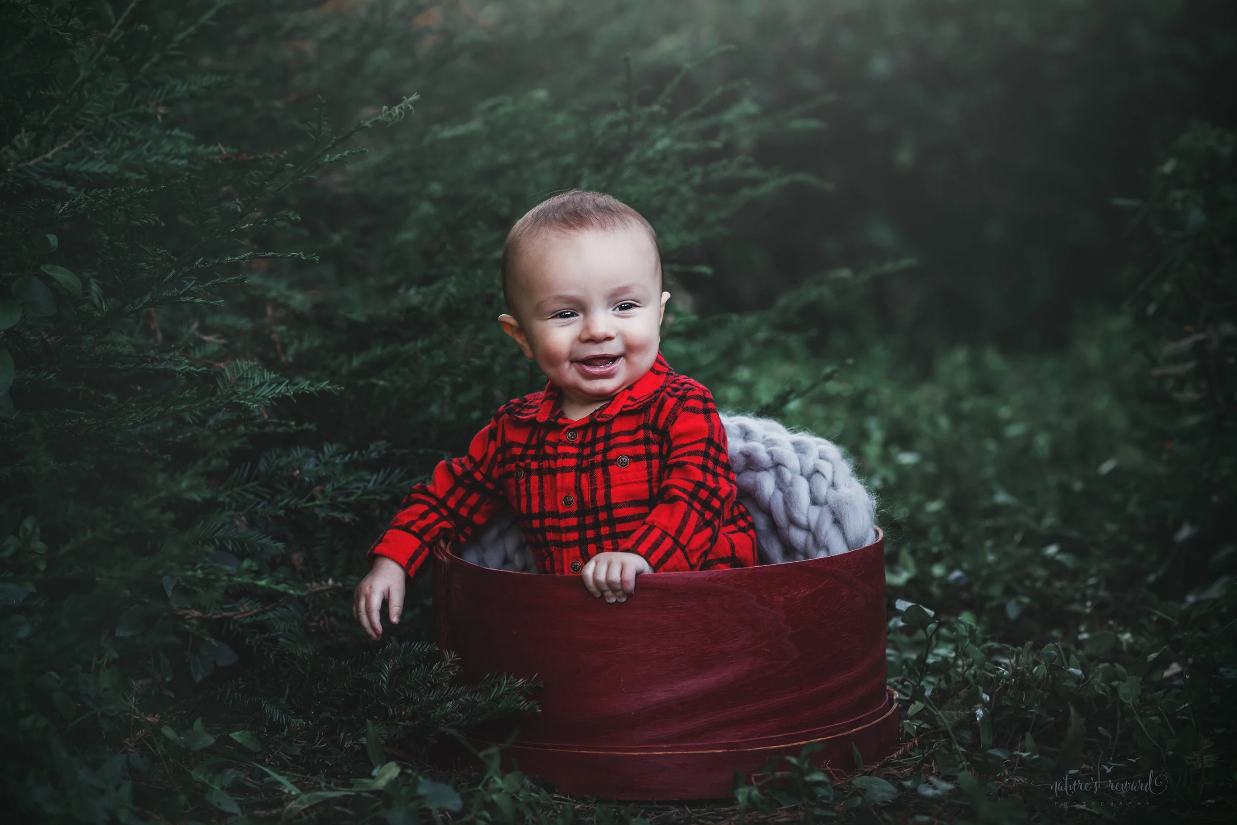 6 Month sitter baby boy in red inside a red circular box in a lush green park setting in Redlands, Ca. by San Bernardino photographer- Nature’s Reward Photography