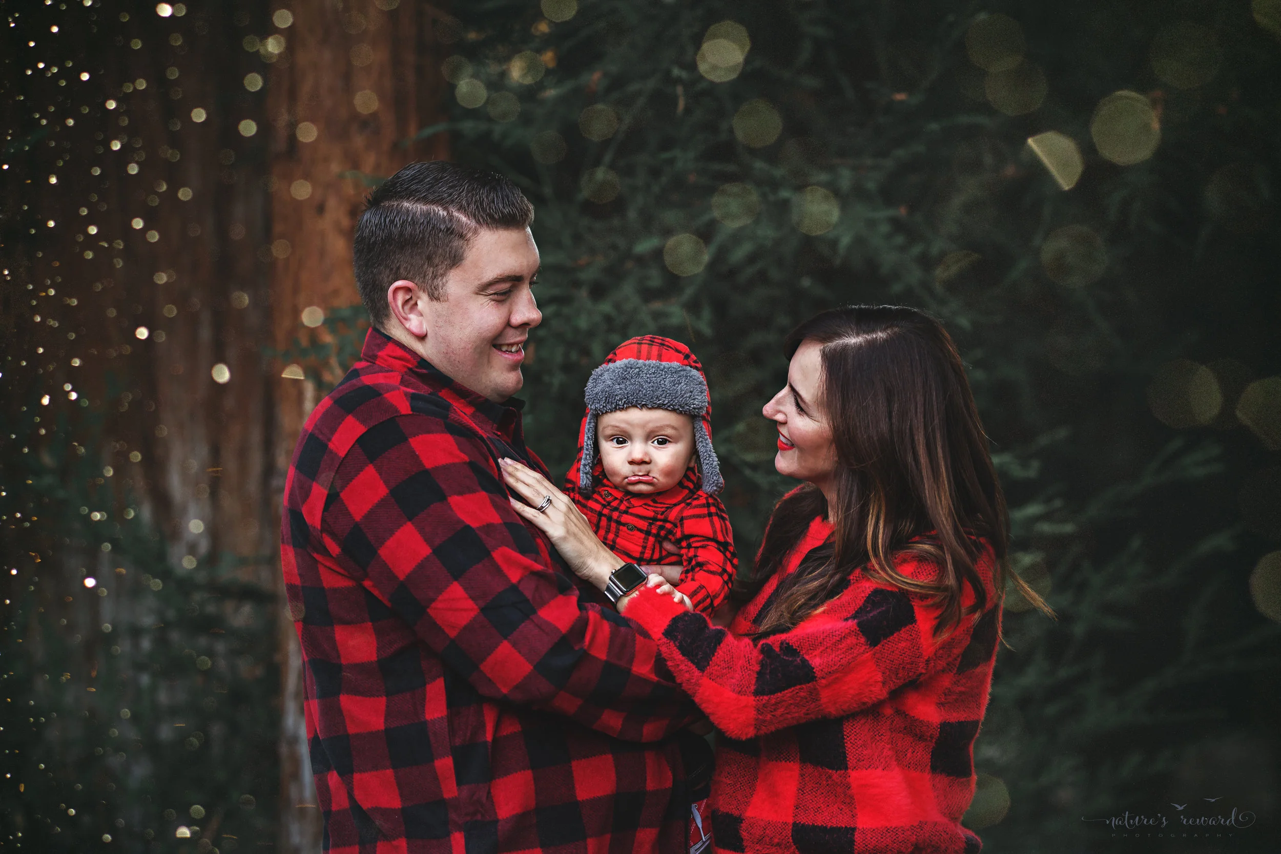Titled- “I Saw Mommy Kissing Santa Claus” 6 month old baby boy with his mommy and daddy in a lush green park setting in Redlands, Ca. by San Bernardino photographer- Nature’s Reward Photography