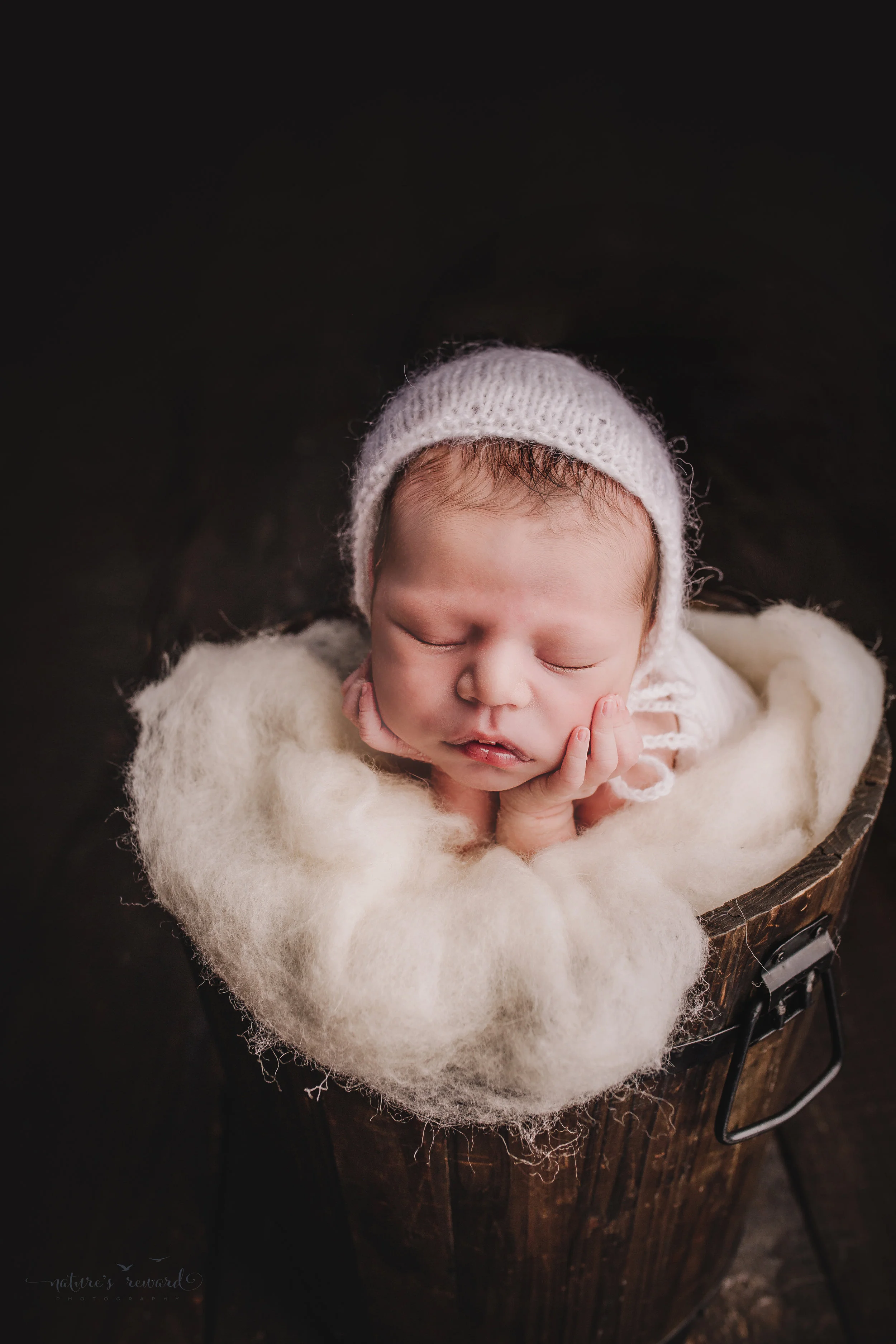 Newborn baby boy swaddled in white in bucket of white fluff on a dark wood floor by san Bernardino’s maternity, newborn and family photography, Nature’s Reward Photography