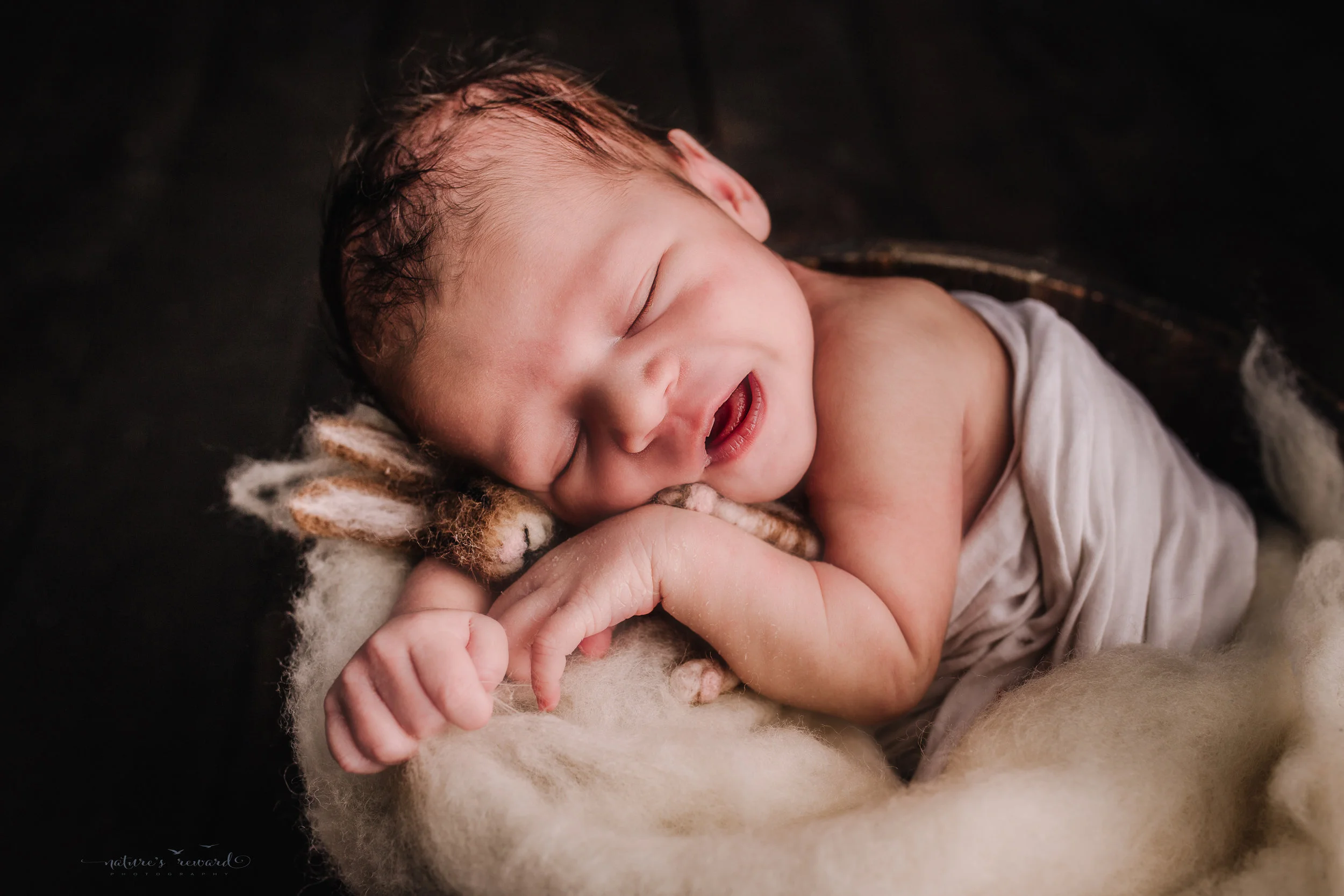 Newborn baby boy swaddled in white in bucket of white fluff on a dark wood floor by san Bernardino’s maternity, newborn and family photography, Nature’s Reward Photography