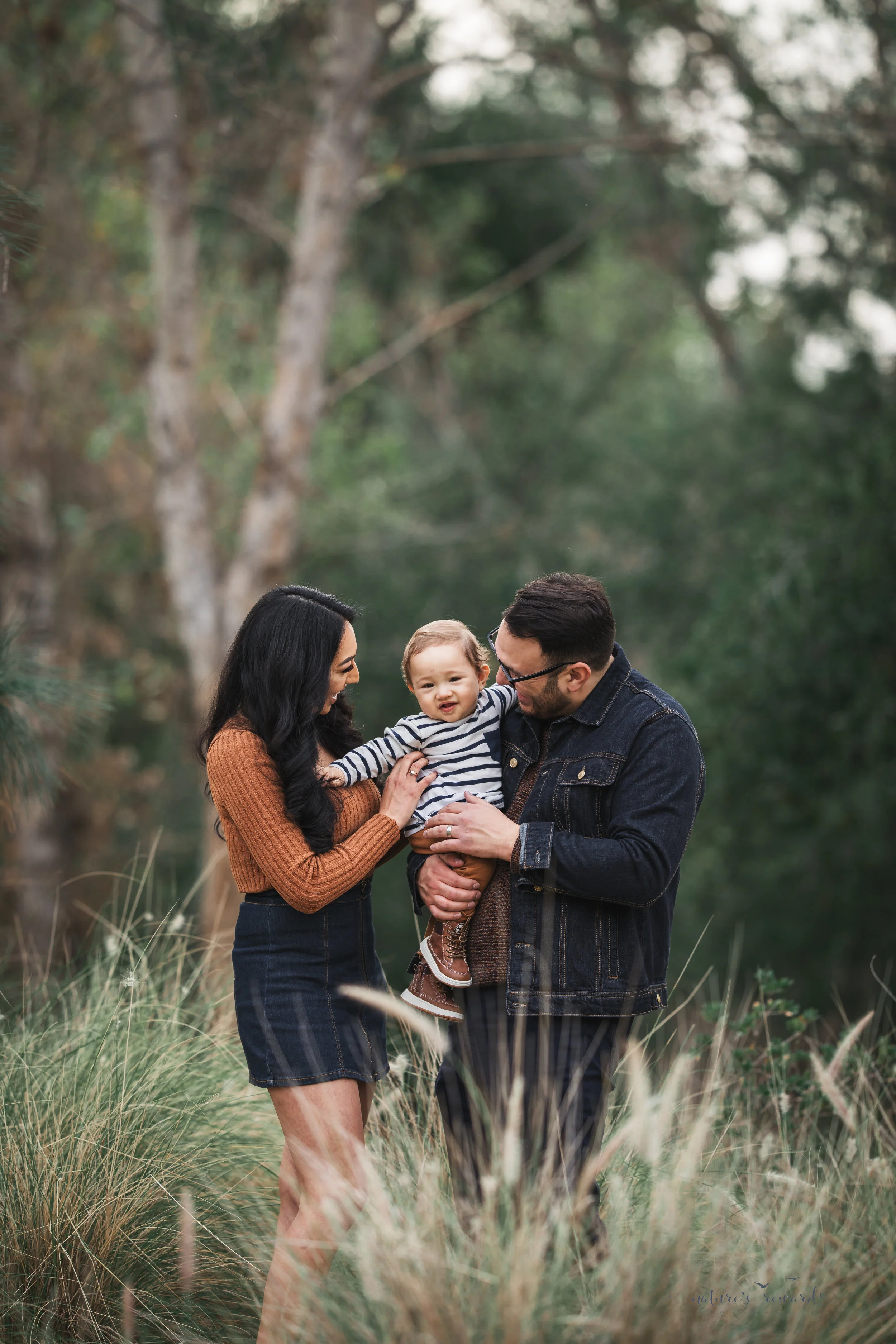 Baby boy in tans and blues with his mother and father in a portrait by Nature’s reward Photography