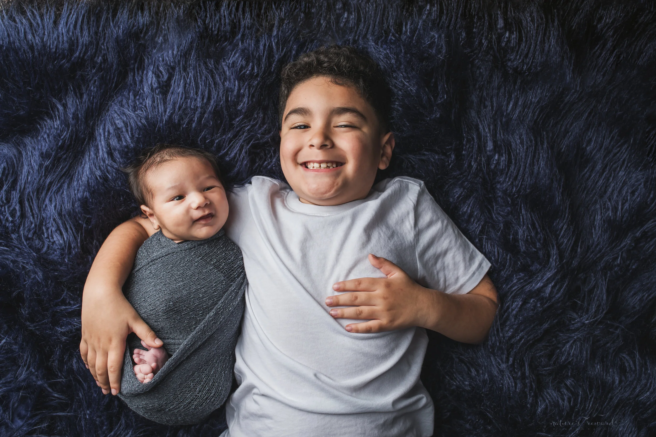 Newborn baby boy swaddled with his brother a portrait by Nature’s Reward Photography