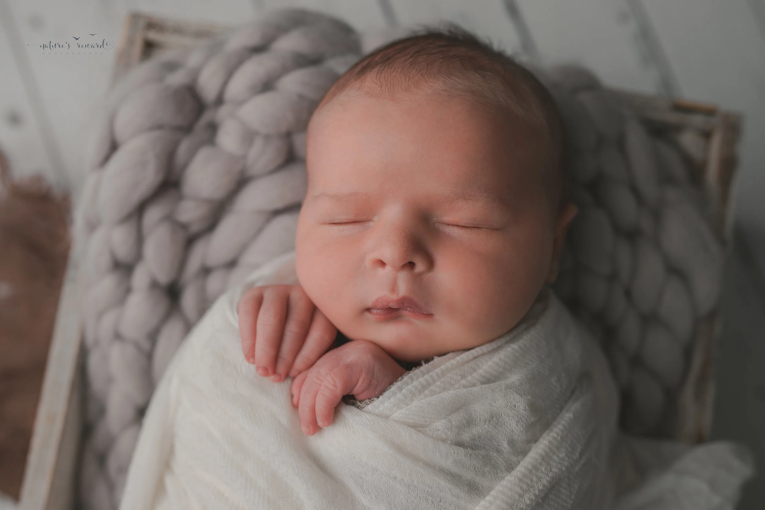 Newborn baby boy swaddled in white, on a white wood floor, resting in a box, a portrait by Nature’s Reward Photography