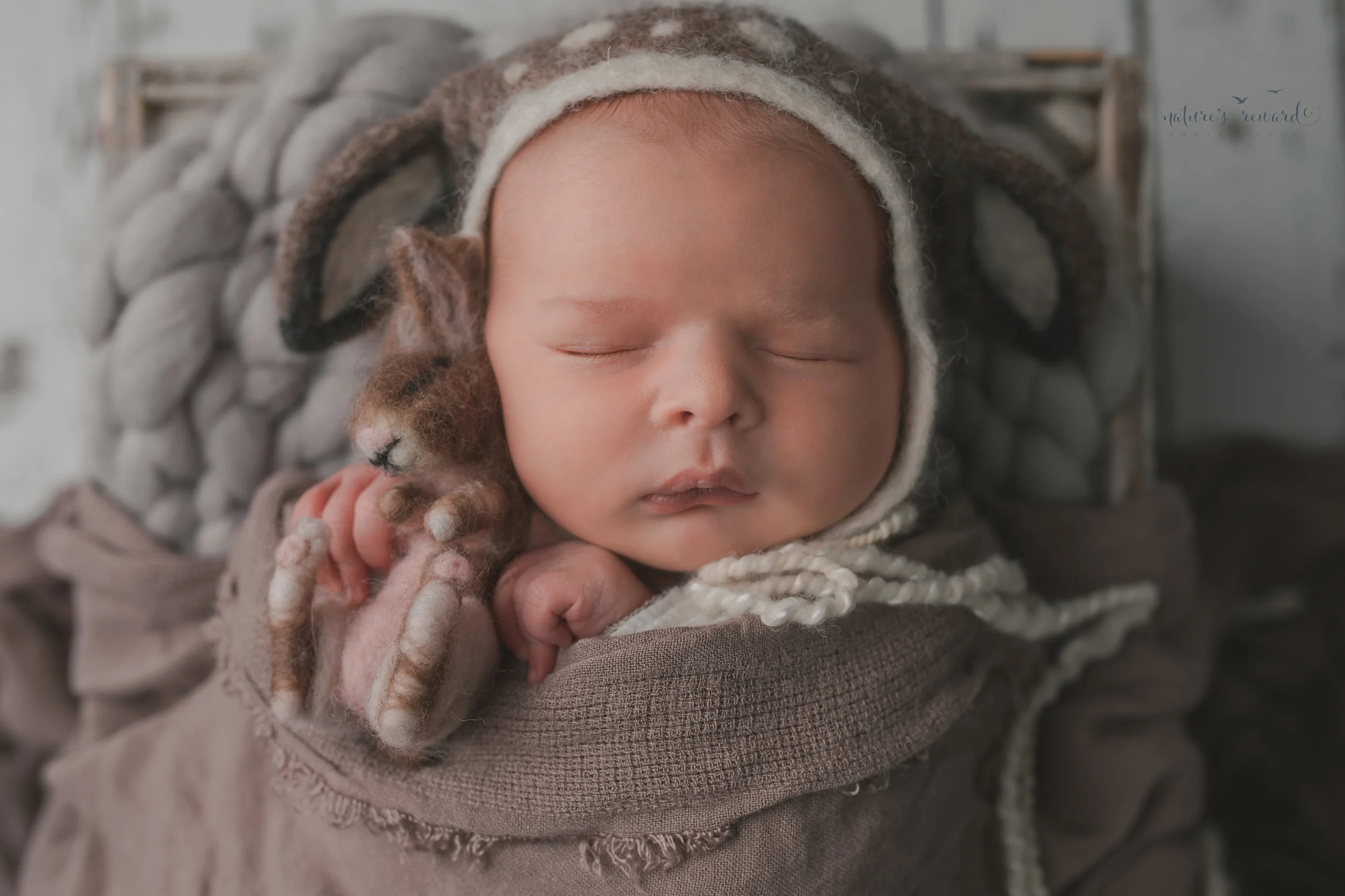Newborn baby boy swaddled brown wearing a deer bonnet holding a bunny, on a white wood floor, resting in a box, a portrait by Nature’s Reward Photography