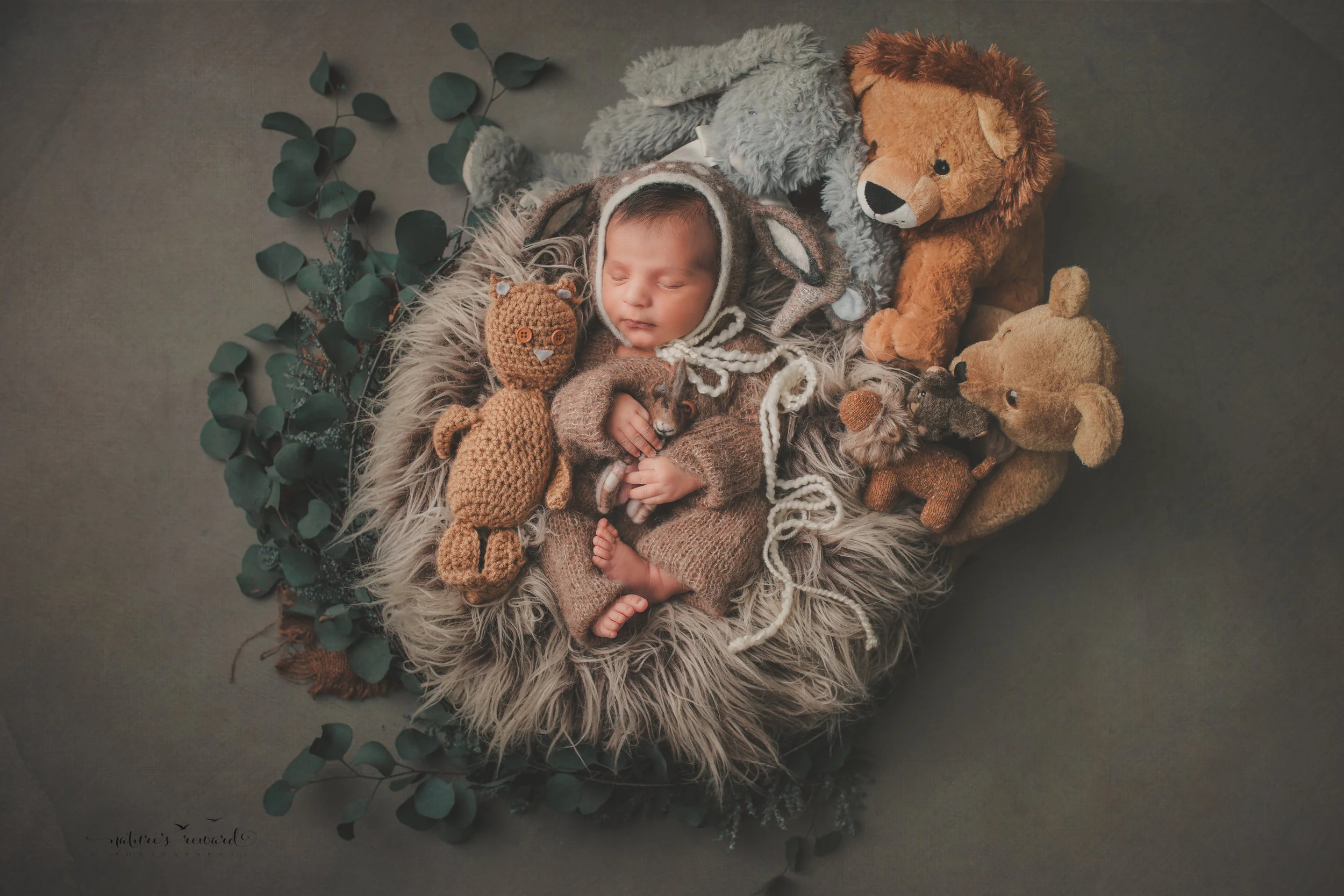 Beautiful baby boy in a deer bonnet with his family of stuffed animals