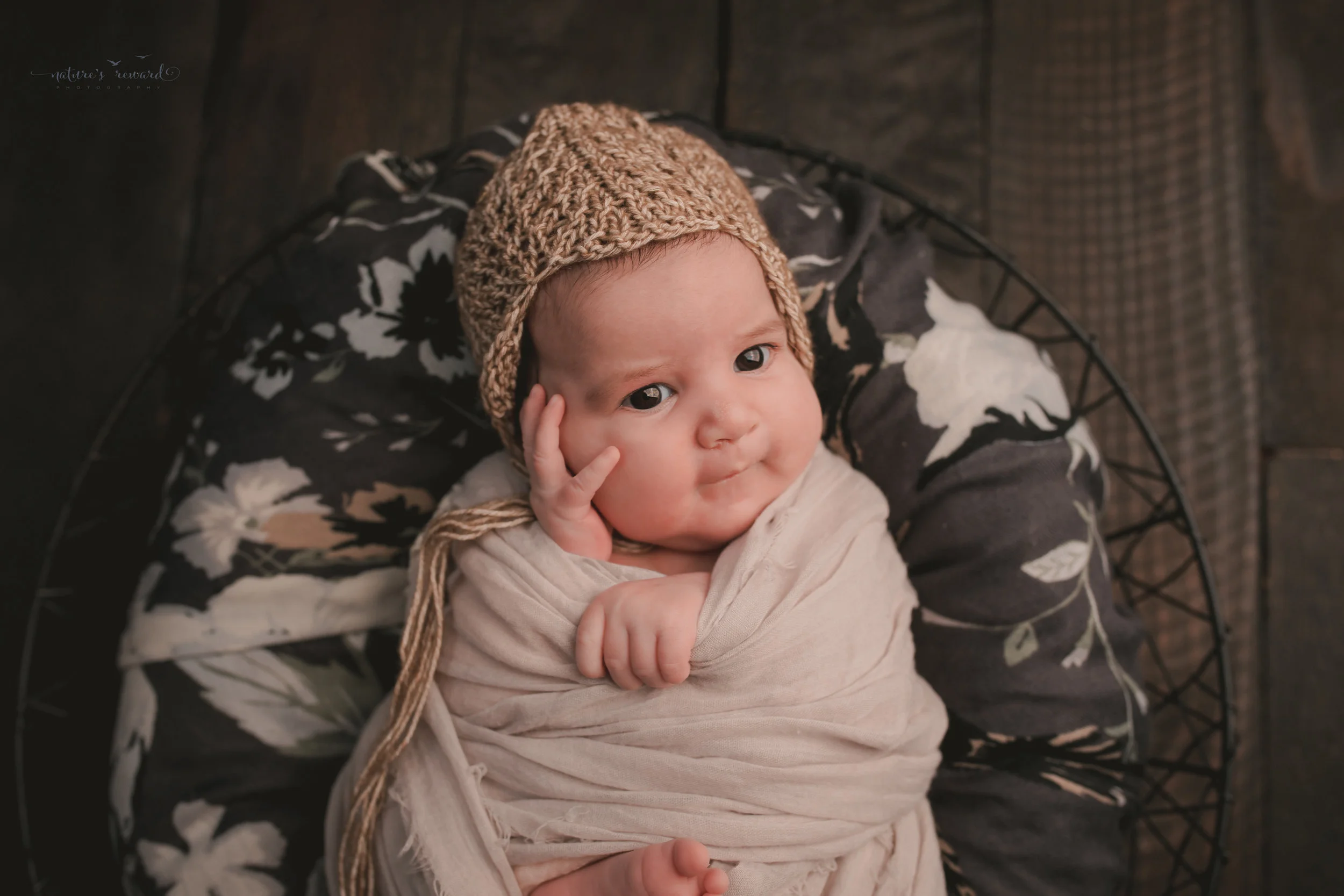 Showing her personality swaddled in lace and laying on grey floral on a wood floor, a newborn portrait by Nature’s Reward Photography