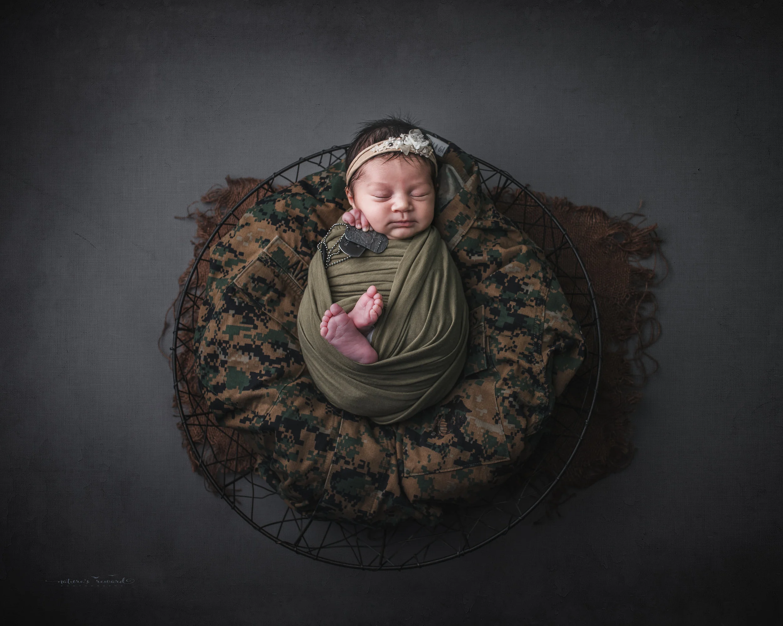 Newborn baby girl swaddled in army green laying on her father’s service uniform with his dog tags, a portrait by Nature’s Reward Photography