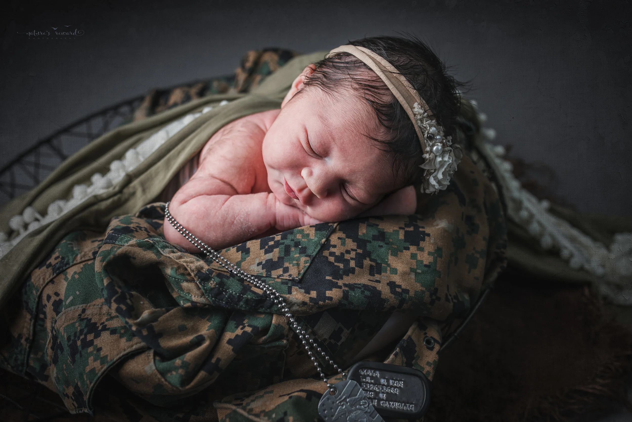 Newborn baby girl in army green laying on her father’s service uniform with his dog tags, a portrait by Nature’s Reward Photography