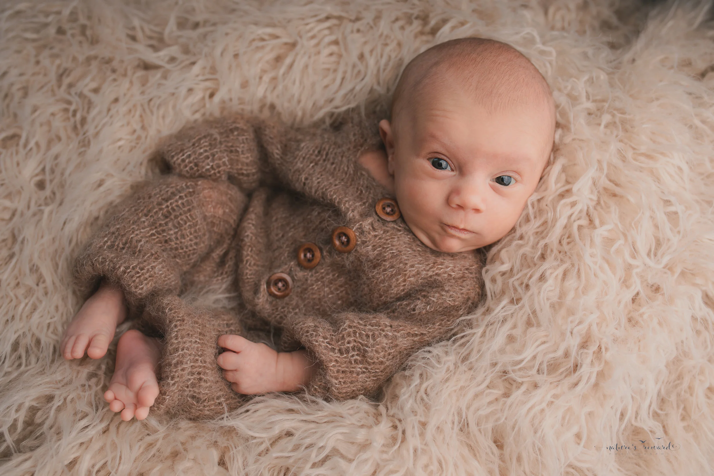 A baby boy wearing a sleeper on a tan fur making a great face by nature’s Reward Photography