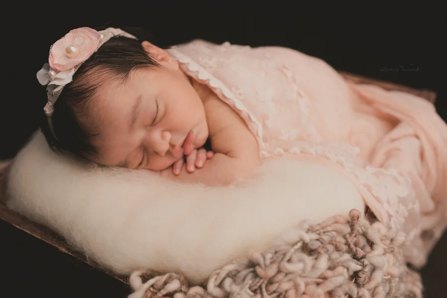 Newborn Baby girl wrapped in pink lace and sitting in a wooden box on a real wood floor in a stunning portrait by Nature’s Reward Photography