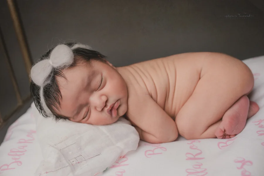 Newborn baby girl on a bed with her name written in the sheet in this portrait by Nature’s Reward Photography