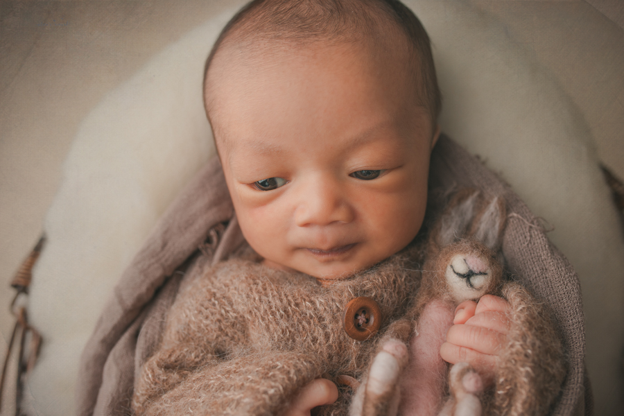 Wide awake in a basket in a cute sleeper holding a bunny in a newborn portrait by Nature’s Reward Photography