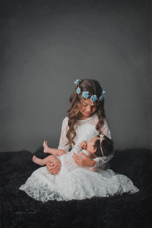 Newborn baby girl and big sister in newborn portrait by Nature’s Reward Photography.