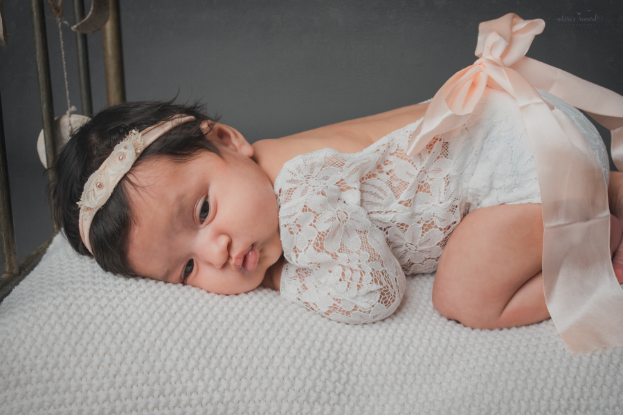 Newborn baby girl on a doll bed surrounded by flowers in this newborn portrait by Nature’s Reward Photography