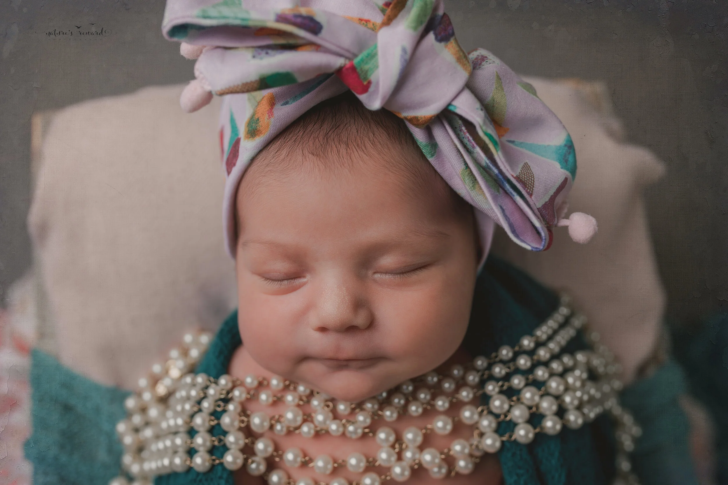 A newborn baby girl in the bow her mother brought for her in this portrait by Nature’s Reward Photography