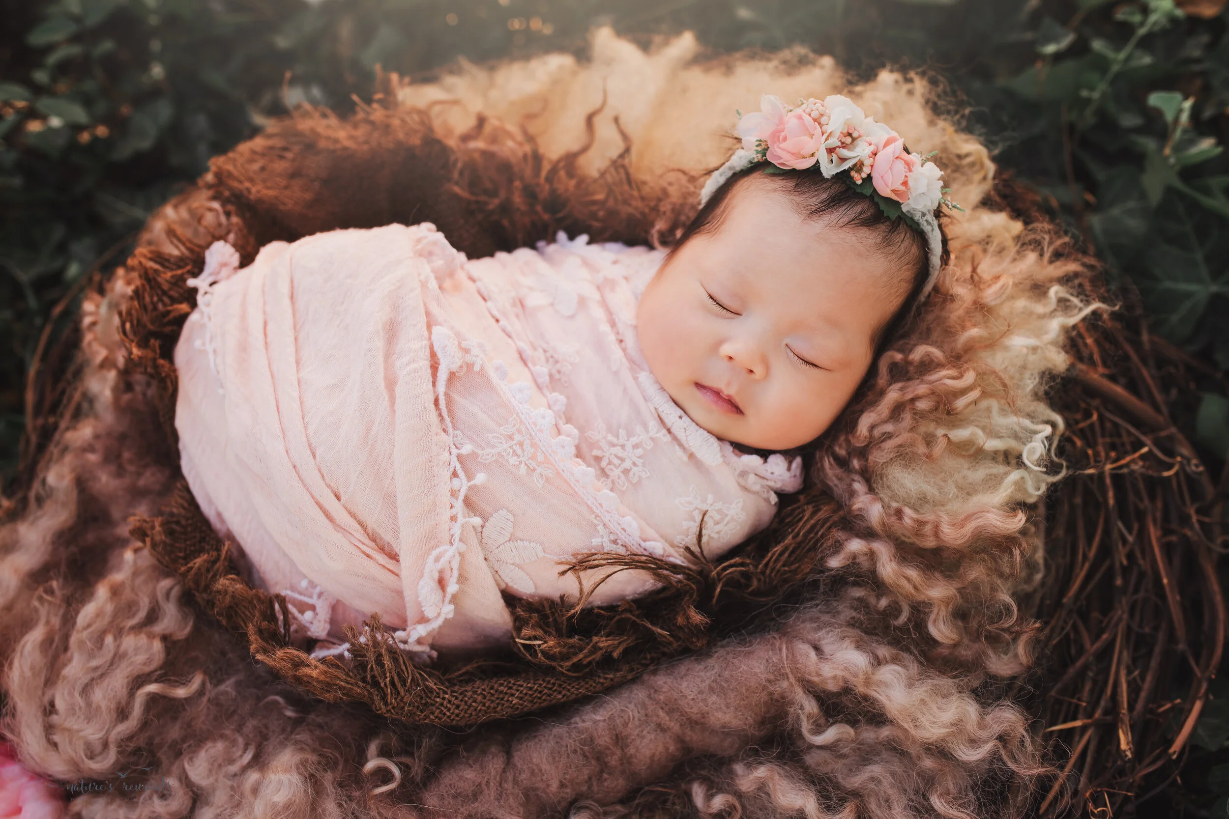 Newborn Baby girl in a pink swaddle in a nest in a garden portrait by nature’s Reward Photography