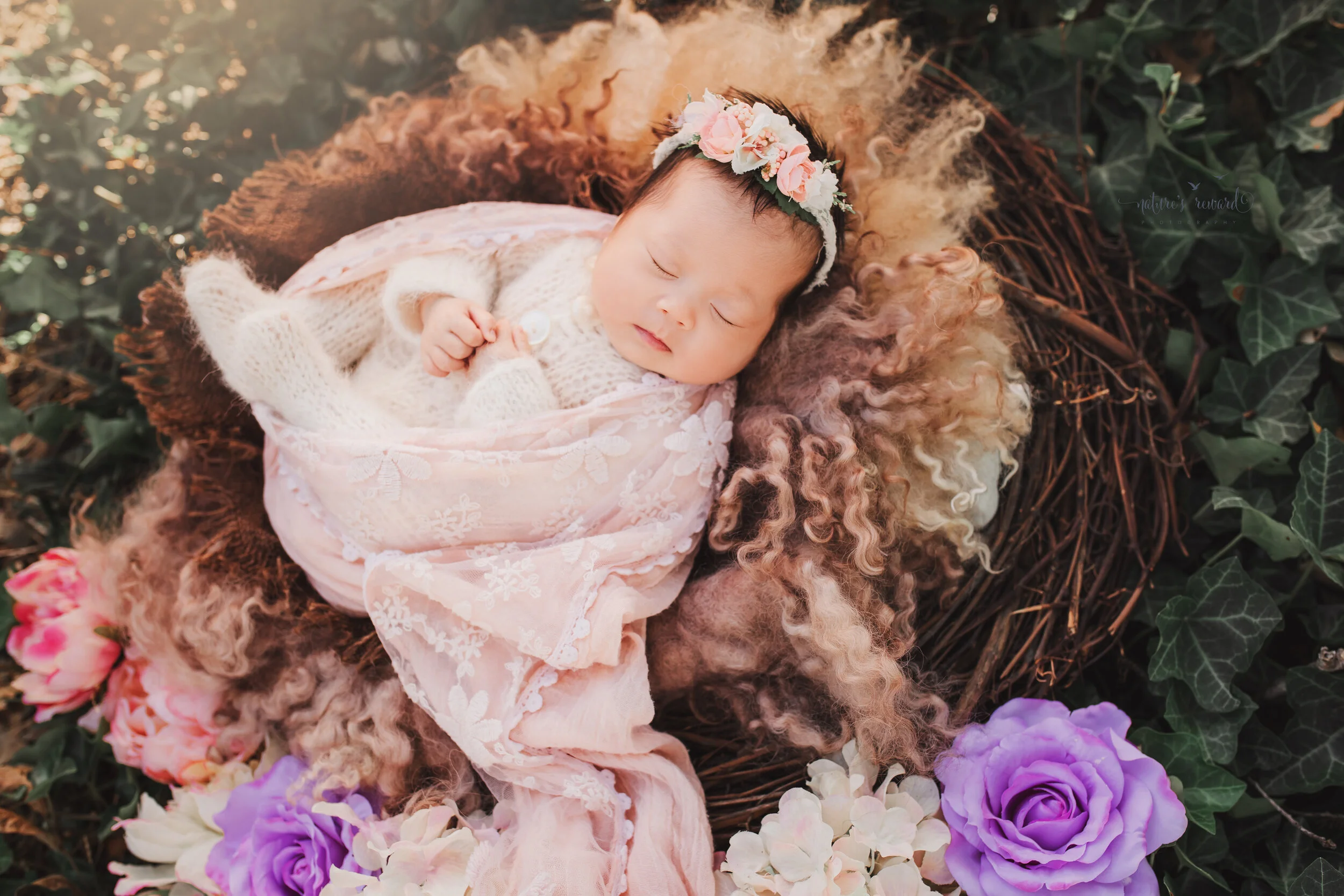 Newborn Baby girl in a pink swaddle in a nest in a garden portrait by nature’s Reward Photography