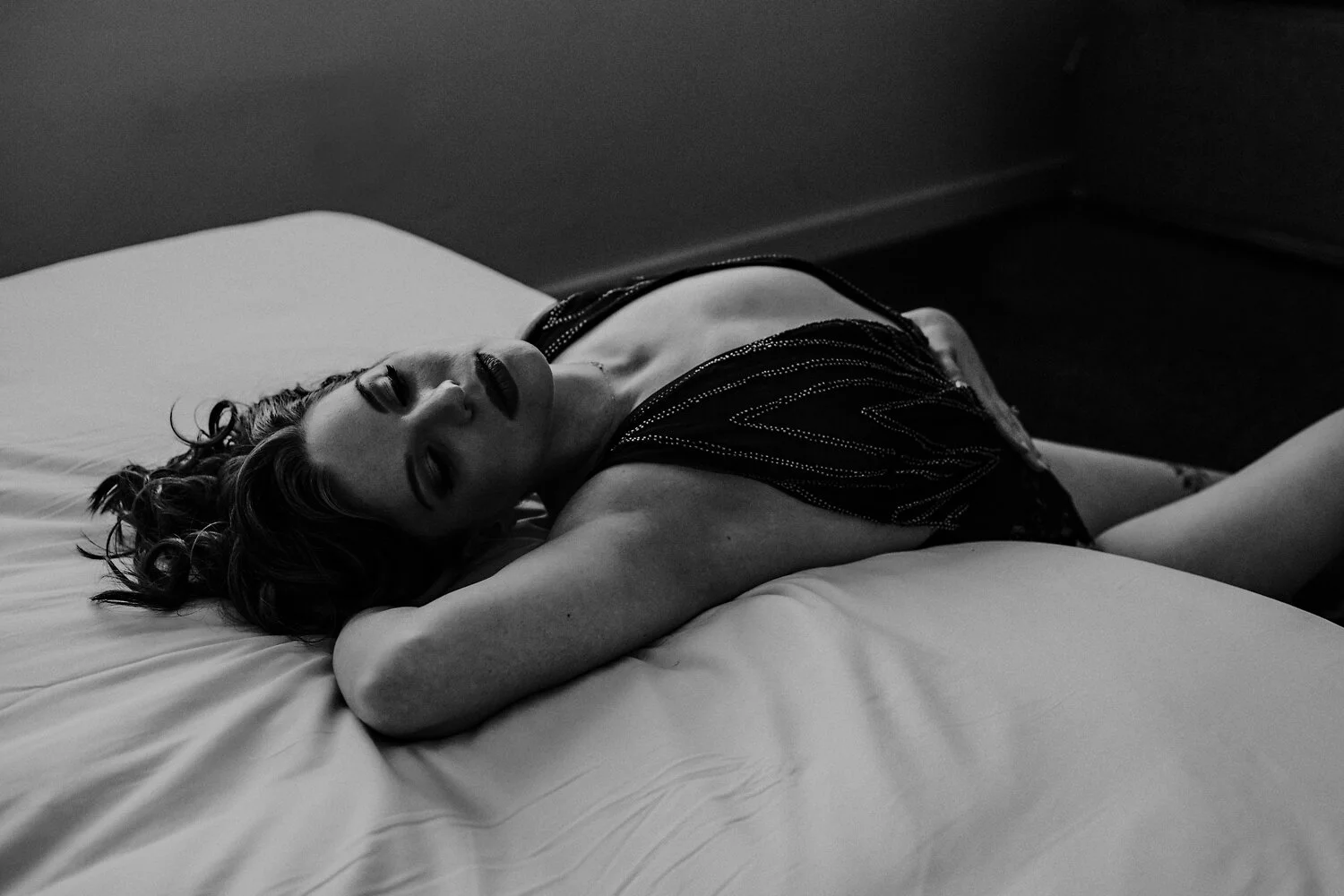  black teddy. boudoir pose laying down on the edge of a bed.  