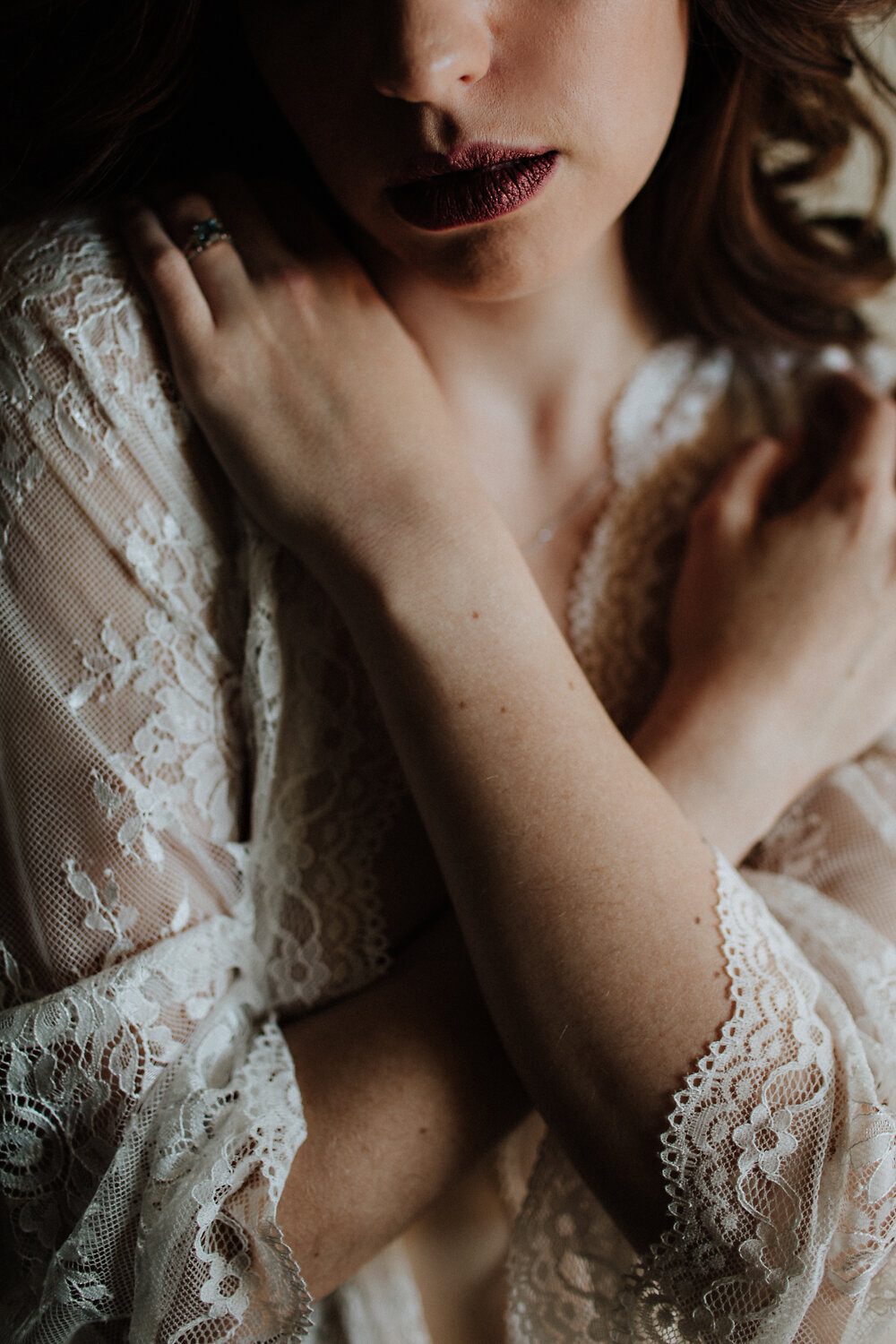  red lips and arms crossed across her chest. detail close up boudoir shot in a white lace bridal robe.  
