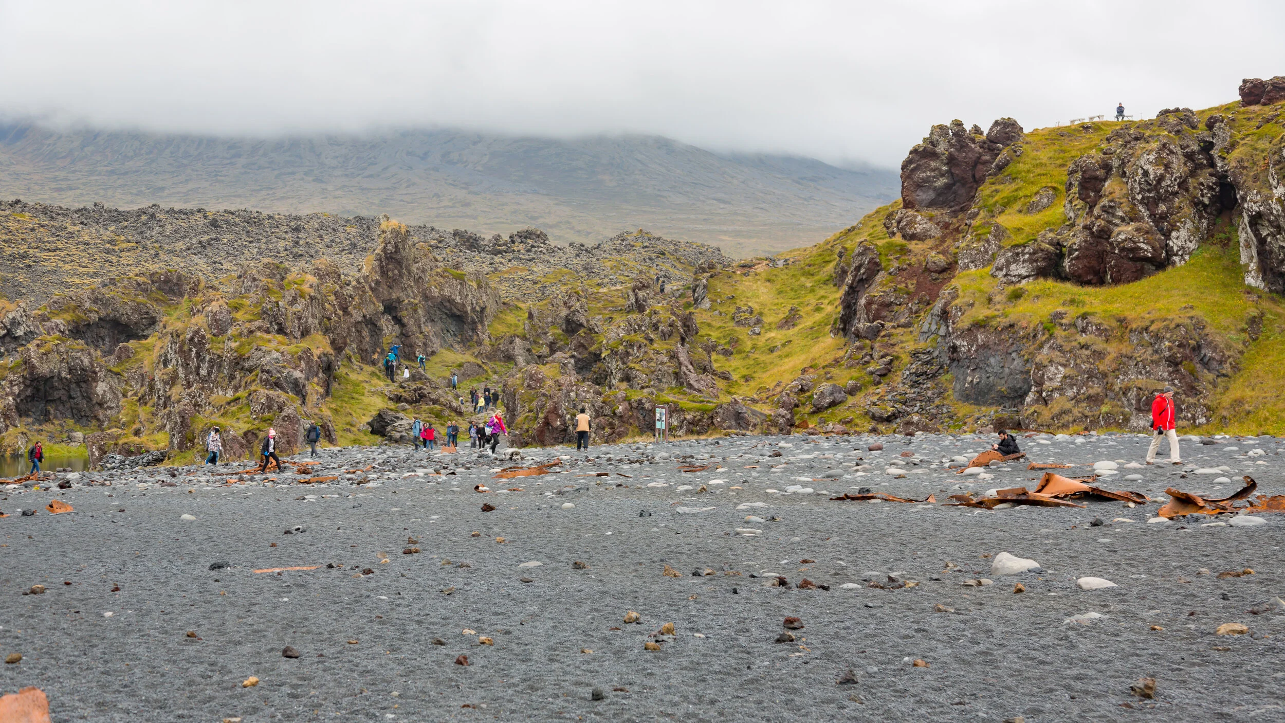  Tourists exploring debris of Edring, a British trawler that wrecked on the beach in 1948, on the Djúpalónssandur beach with the beautiful green cliffs 