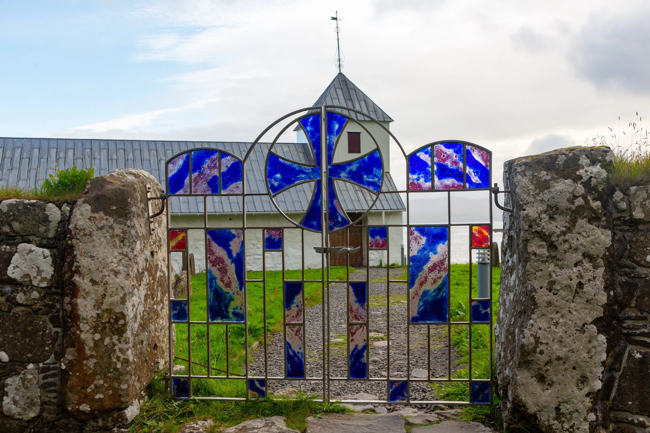  Saint Olav's Church in Kirkjubøu, with a unique metal gate featuring stained glass and blue and red motifs 