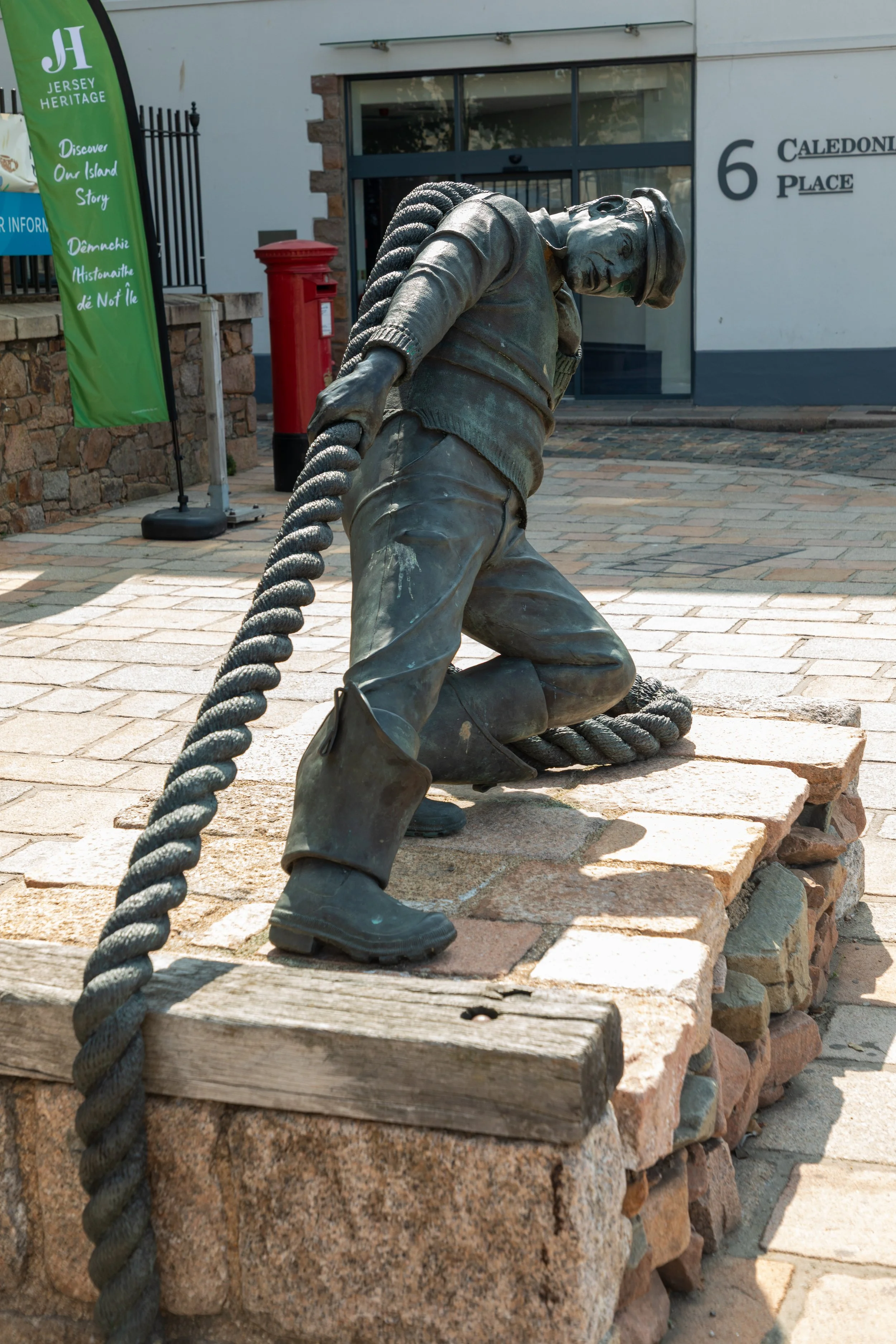  "La Travailleux D' Cauchie" or "The Docker" statue, near the entrance to the Jersey Museum, depicts a dock worker pulling on a thick rope 