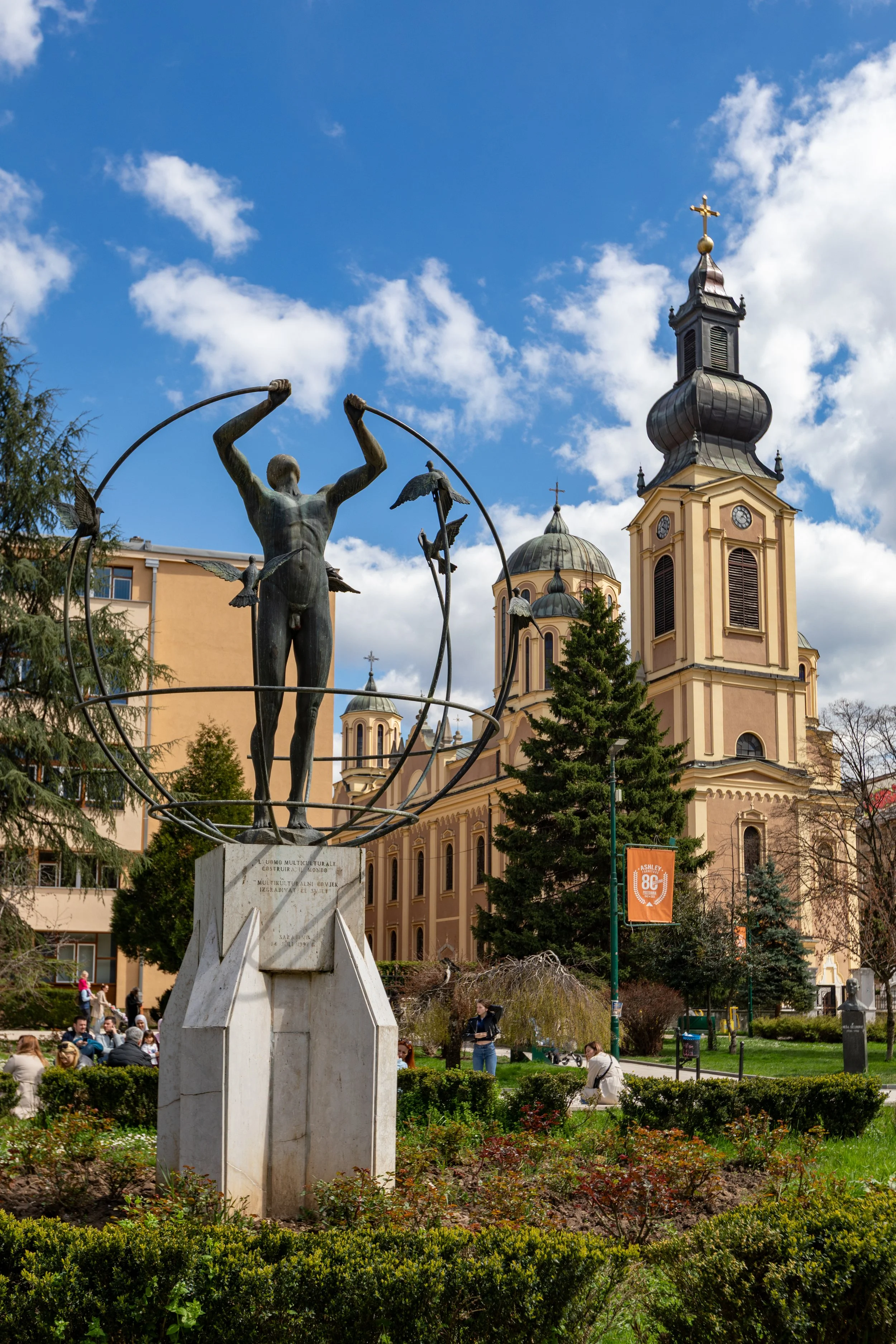  "Multicultural Man Builds the World" sculpture in “Liberation and Izetbegović Square” with the Serbian Orthodox Cathedral of the Nativity of the Theotokos in the background 