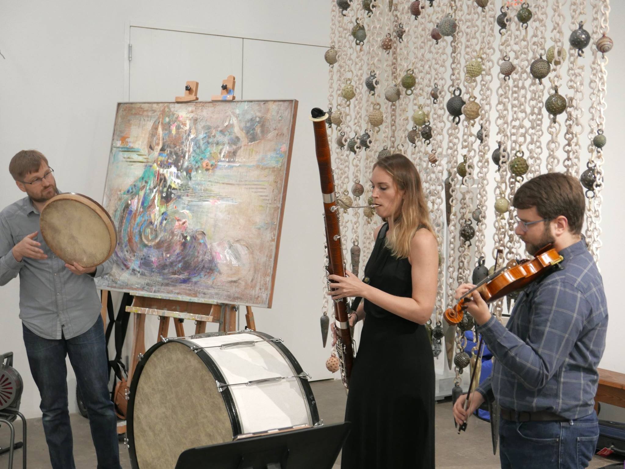 A Percussionist, bassonnist, and violinist performing in front of artwork