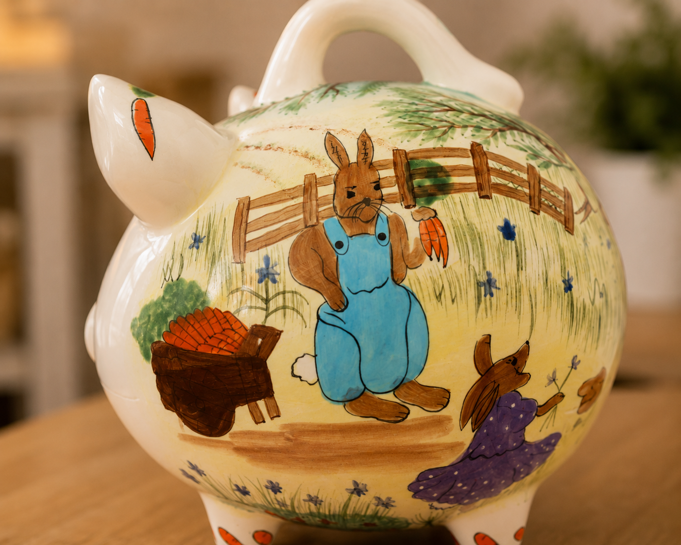 Hand-painted Country Bunnies ceramic piggy bank with charming rabbit and carrot artwork, displayed in a garden with bunnies and fresh carrots.
