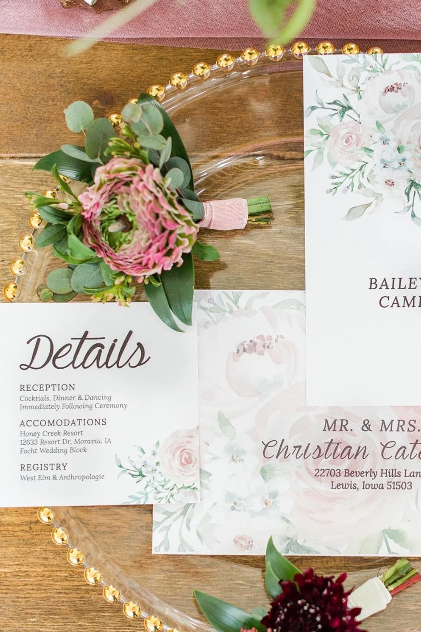Close-up of a wedding reception invitation with floral accents, placed on a wooden table next to a small bouquet of flowers and a decorative beaded plate edge.