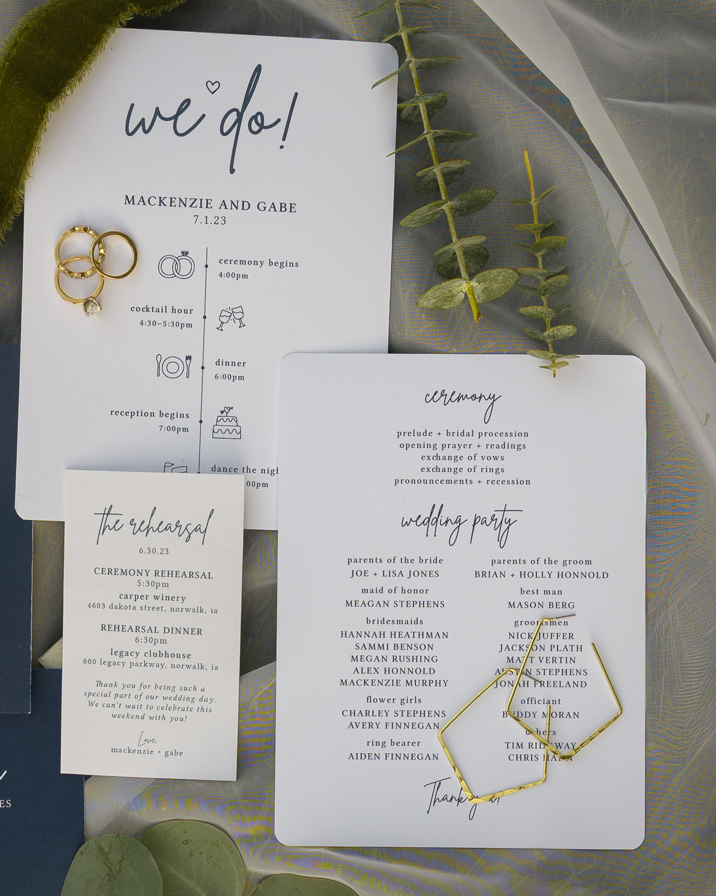 Wedding program and rings on a decorative surface with greenery and a gold paperclip.