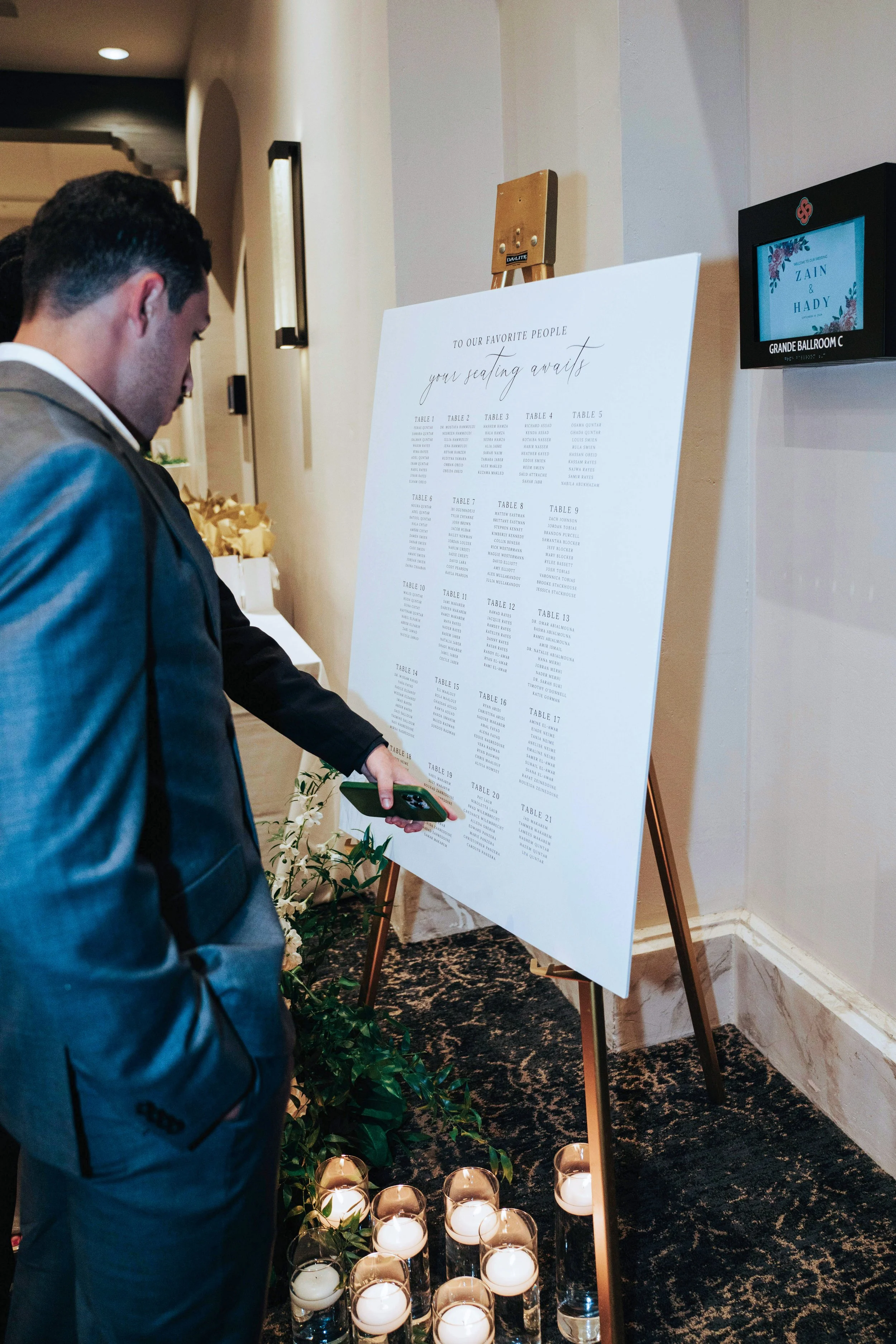 Man in gray suit looking at a table seating chart at an event, with lit candles at the base of the board.