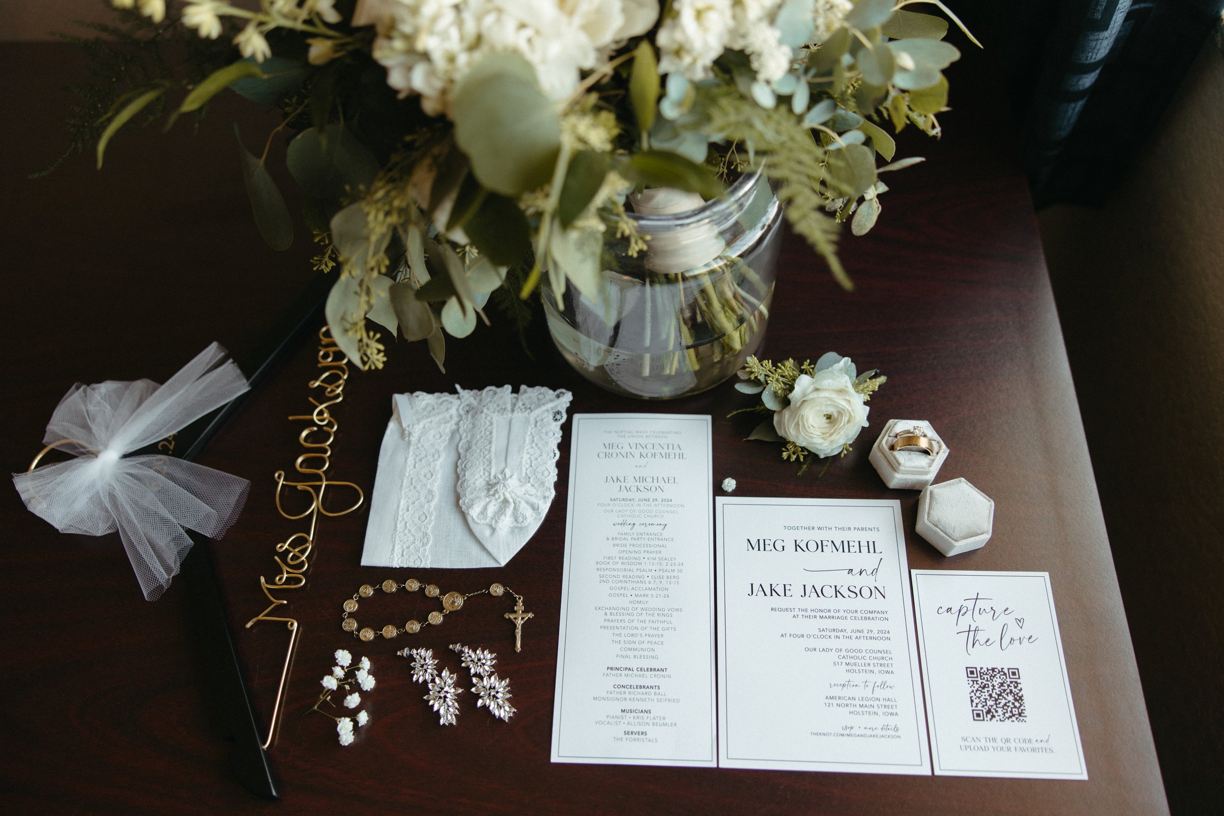 Wedding reception table with floral arrangements, wedding invitation, jewelry, and wedding accessories.