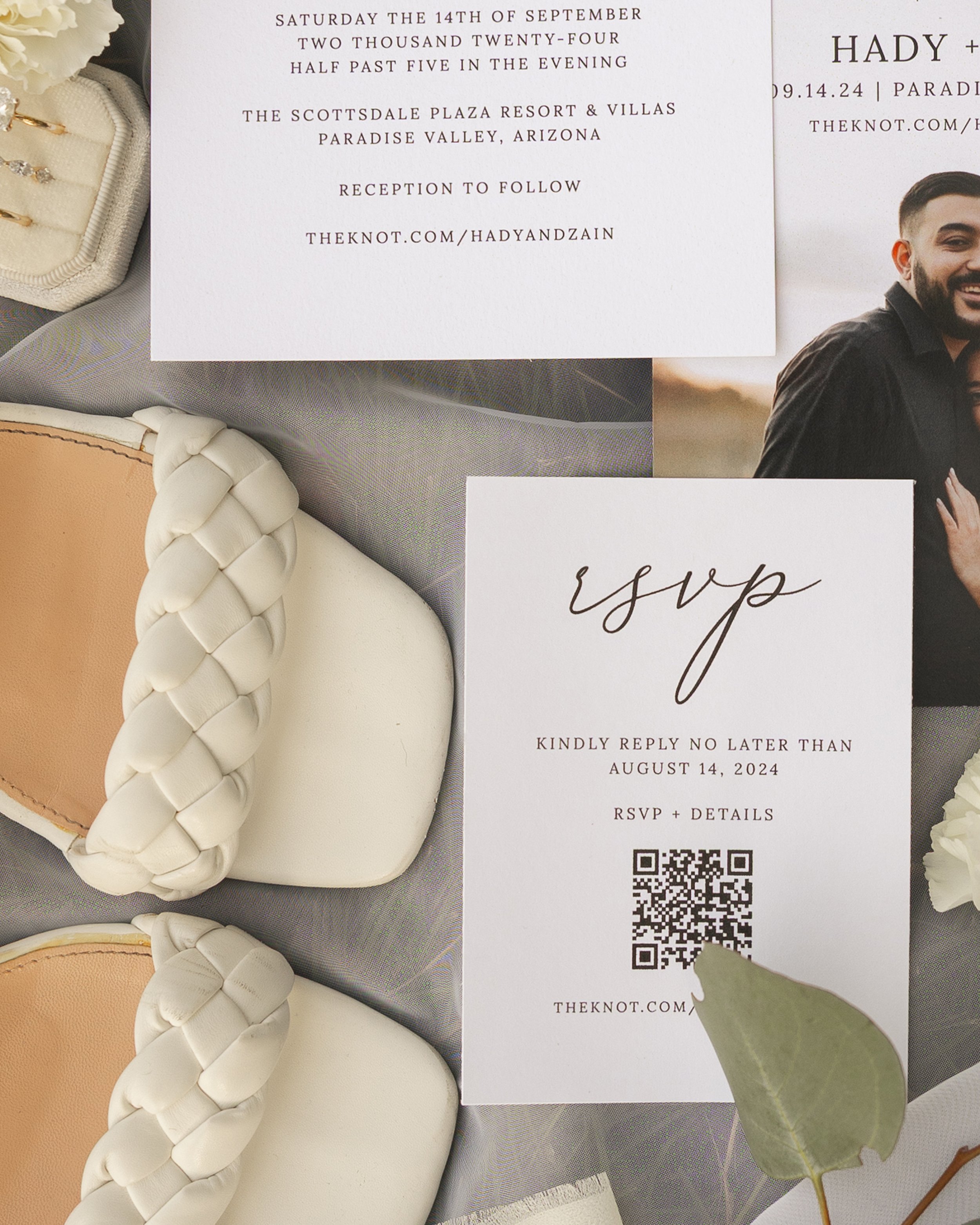 Wedding invitation with details about the date, time, location, and RSVP information, surrounded by jewelry and greenery.
