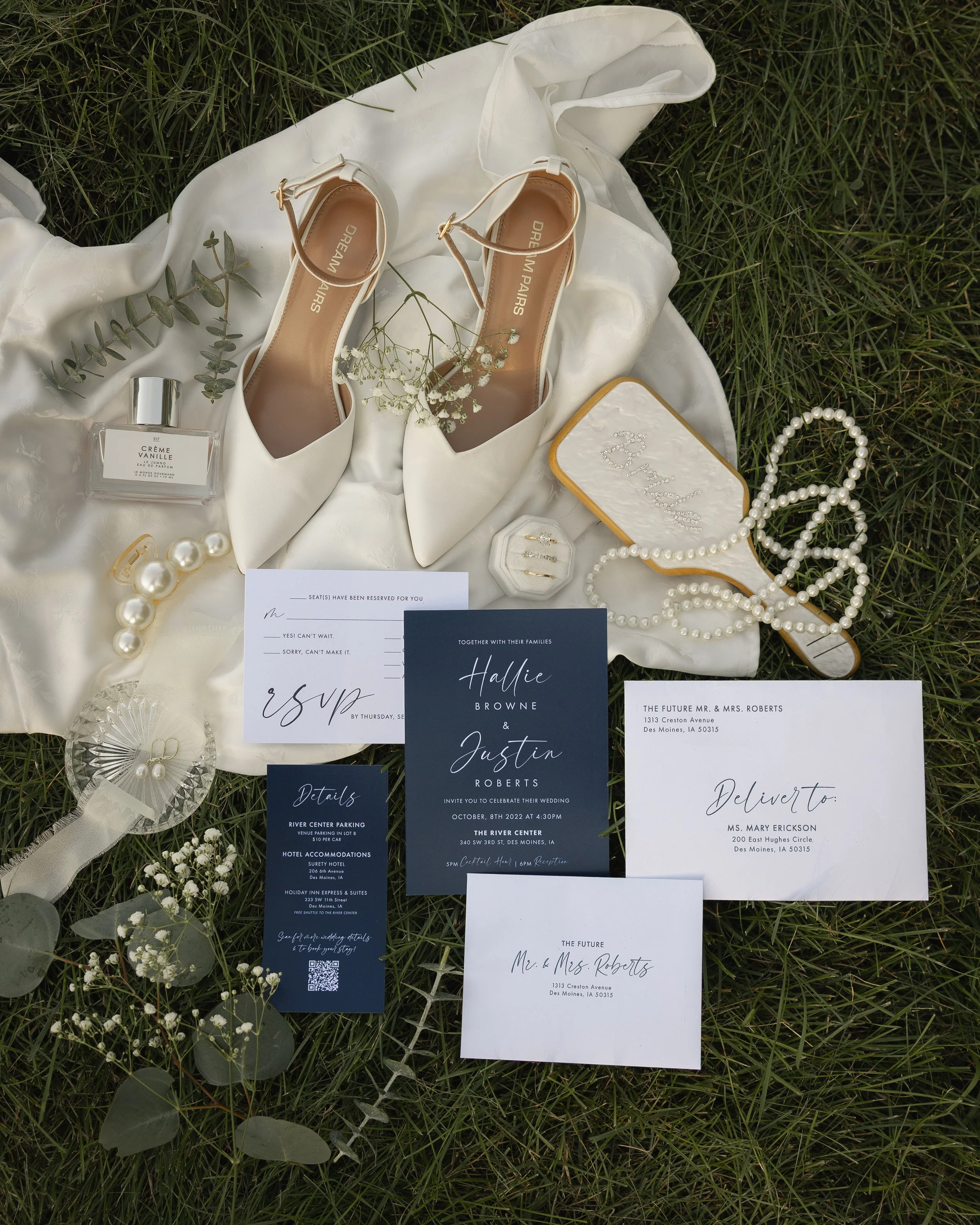 Wedding invitation cards, shoes, perfume, pearls, and decorative flowers arranged on grass for a wedding celebration.