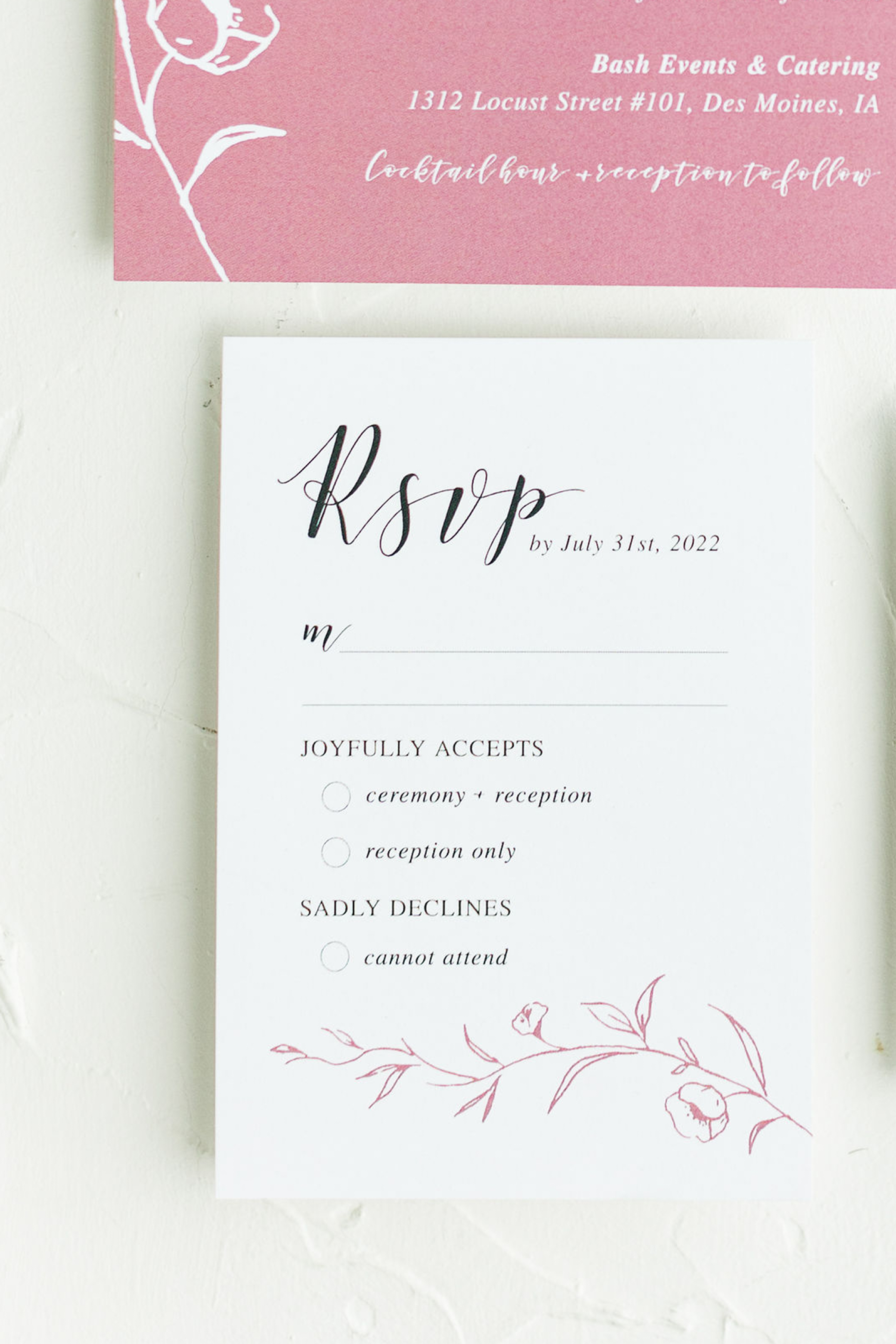 Close-up of a wedding RSVP card with elegant cursive and printed text, featuring floral illustrations at the bottom.