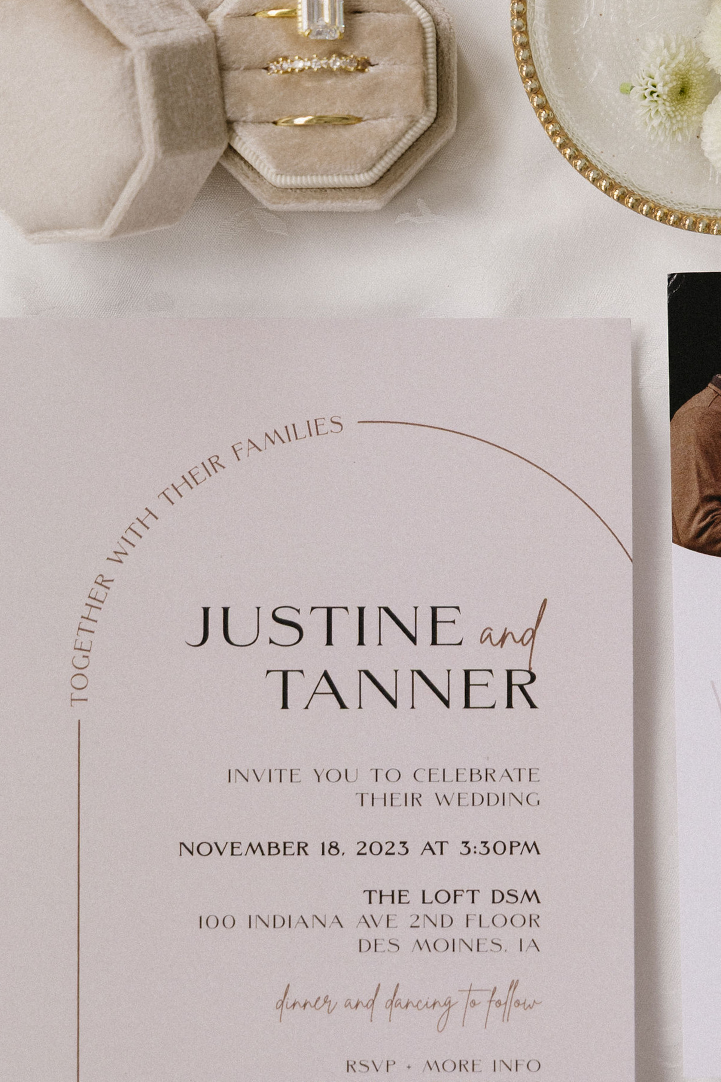 A wedding invitation card with the names Justine and Tanner, details about the date, time, and location of the wedding, and decorative elements. The image also includes a jewelry box with rings and a glass with flowers.