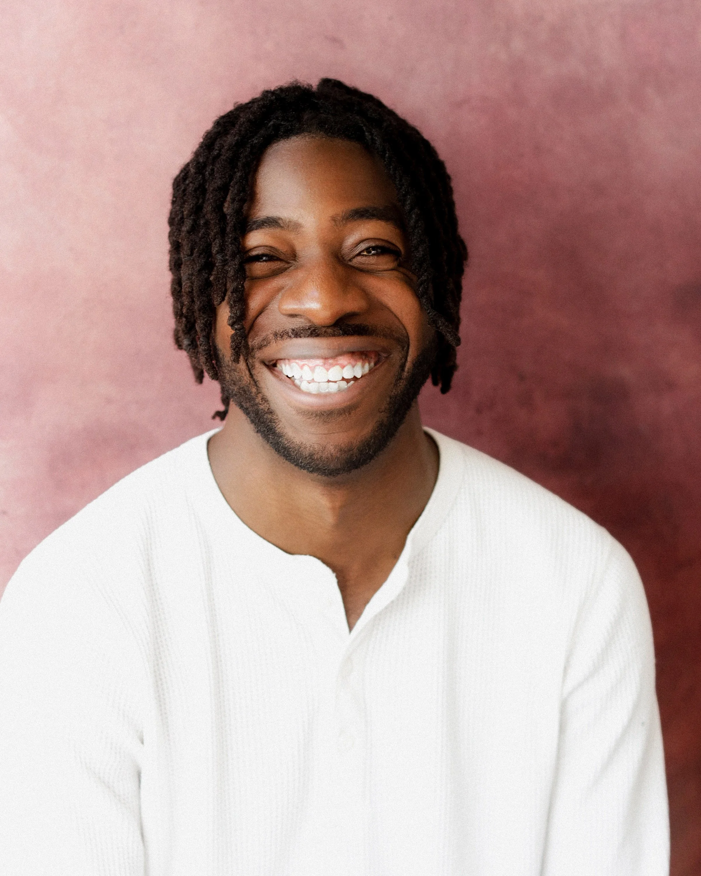 Jeremy Zinunu, French actor and filmmaker — headshot with a wide open laugh against a dusty pink backdrop, photographed by Kirill Kozlov, North London.