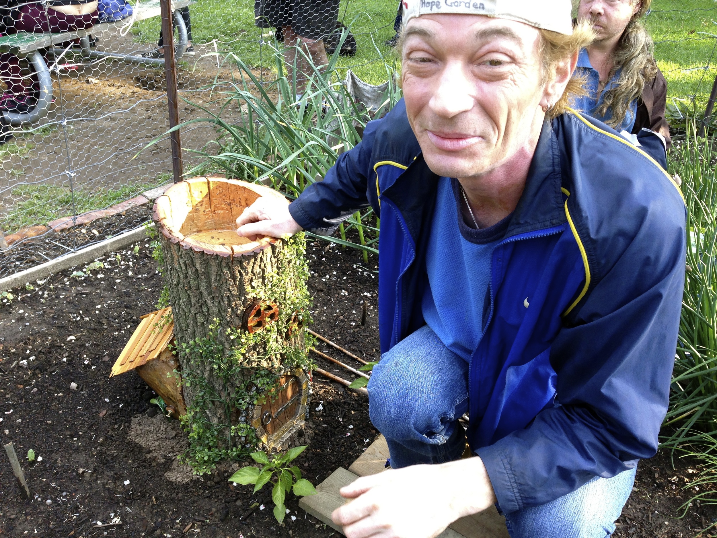  A gardener crouching next to a decorative log in the Dunn Parkette Learning Garden 