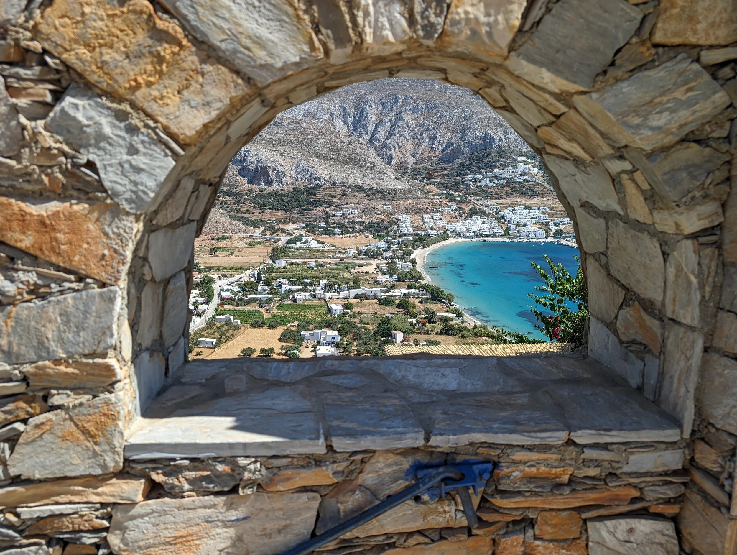 View of the Aegean Sea and coastal village on Amorgos Island, Greece, framed by a traditional stone archway during an Outer Banks Yoga wellness retreat.