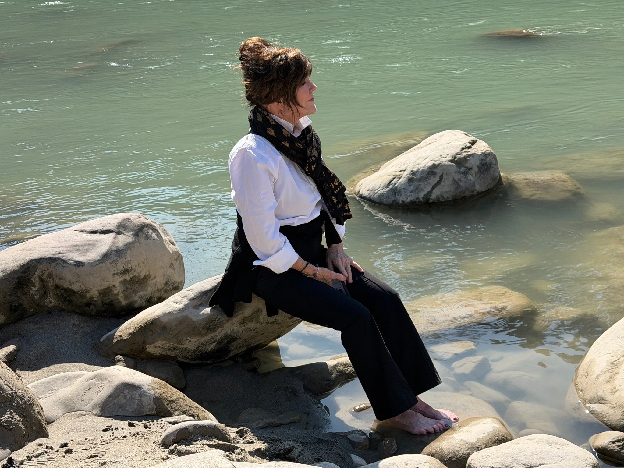 woman meditating on rock with her feet in the ganges river during a yoga retreat.