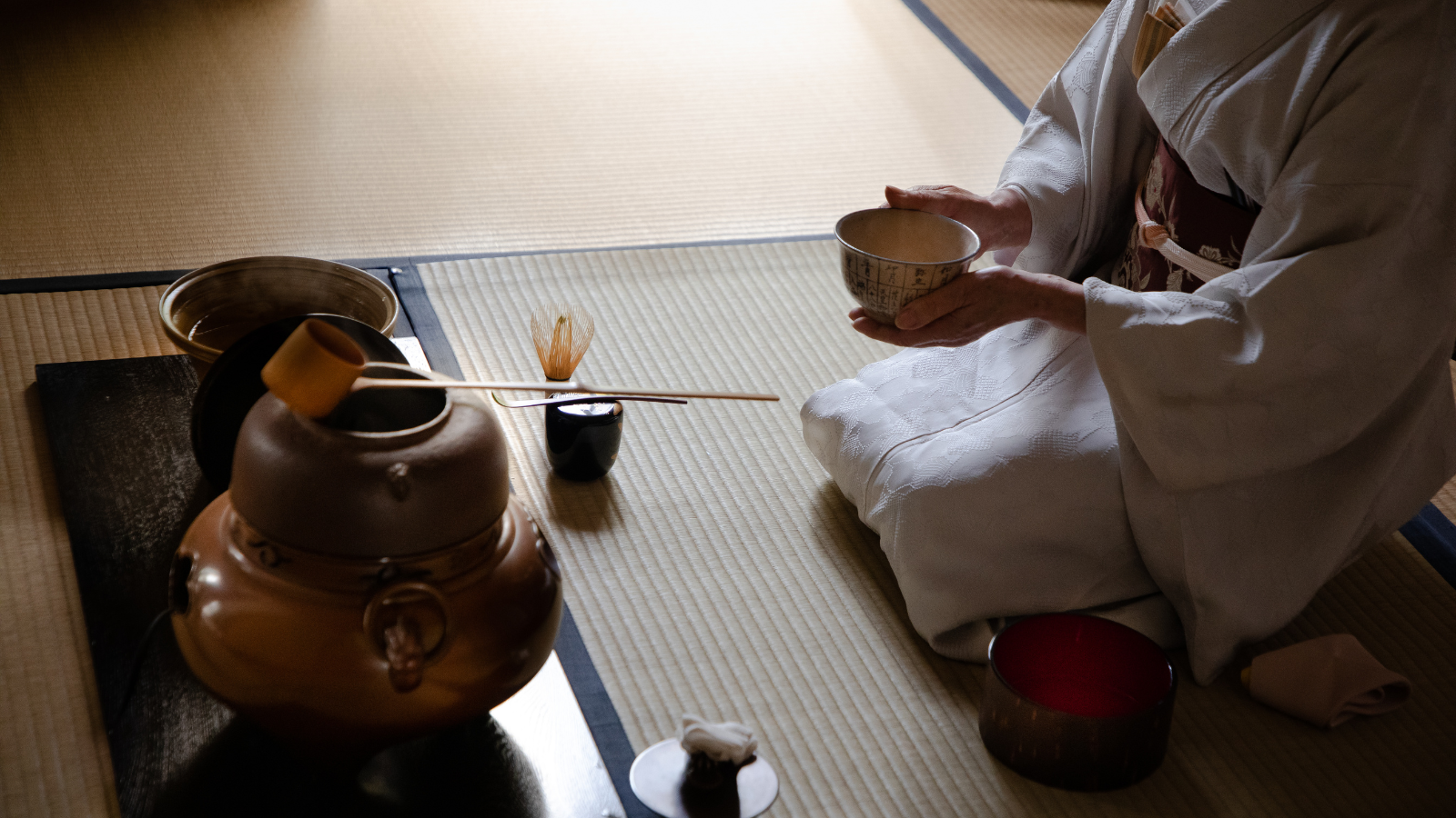A Japanese woman in a traditional kimono performing a mindful tea ceremony preparation with a iron kettle in Kyoto.